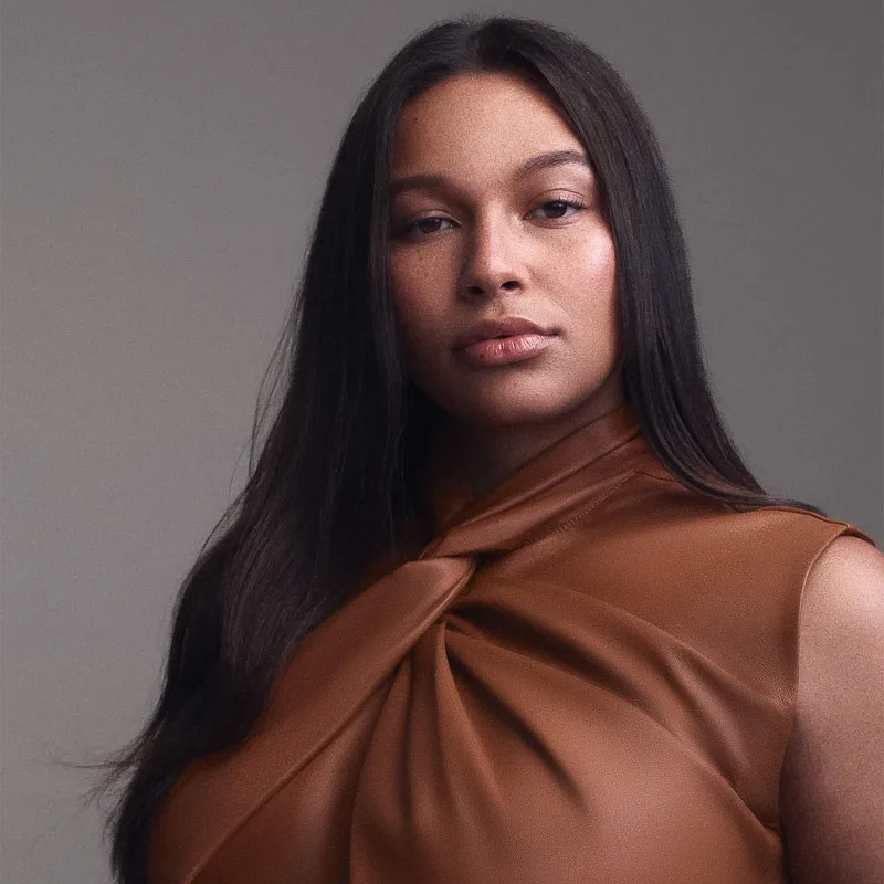 Woman with long, sleek dark hair in a tan twist-neck satin top against a grey backdrop, for Cecred.