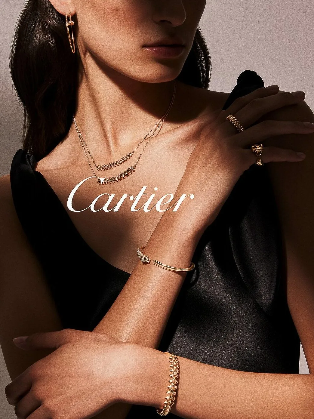 Model in a black satin dress wearing gold hoop earrings, layered necklaces, rings and bracelets, for Cartier.