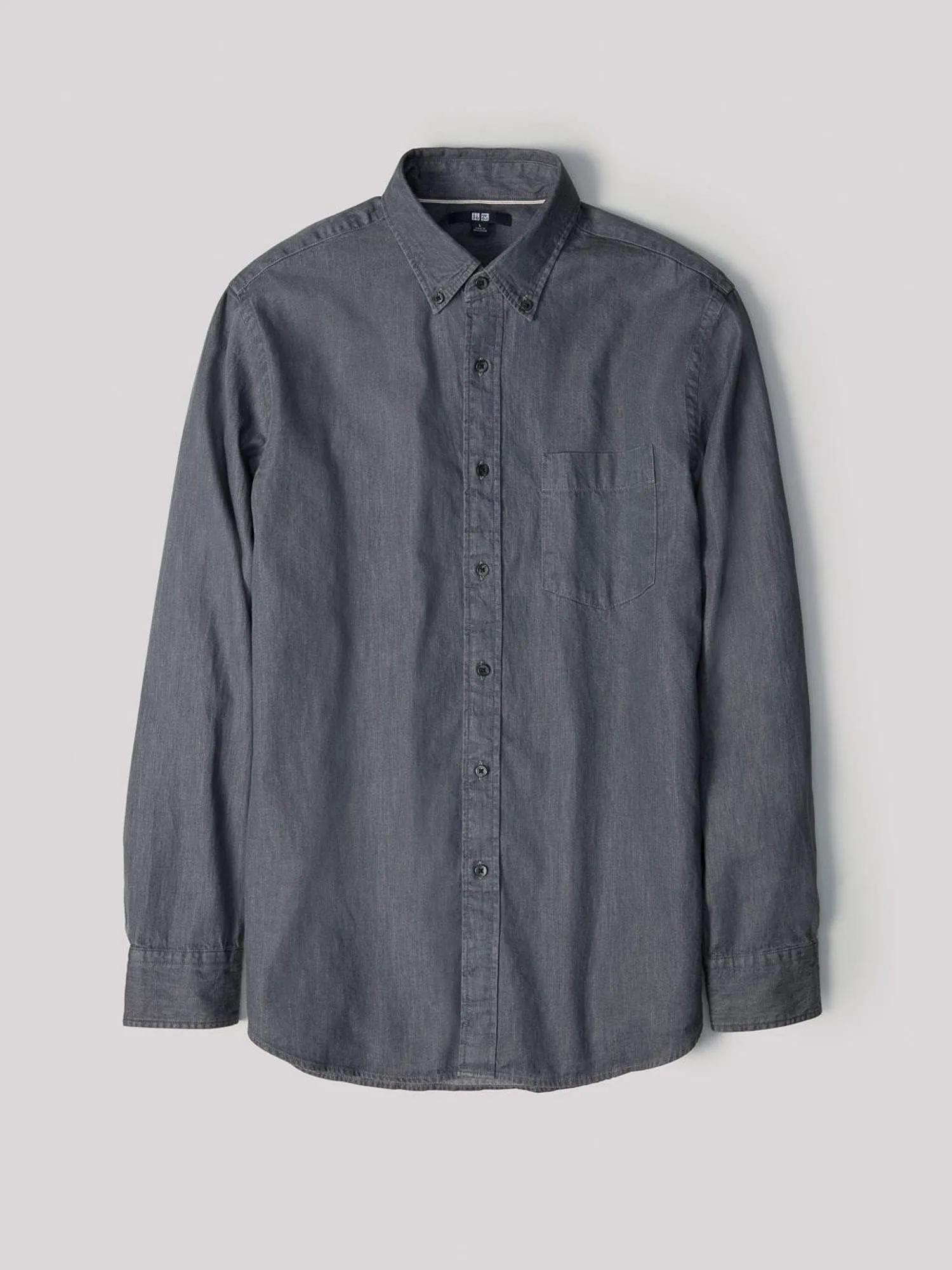 Grey chambray long-sleeve button-down shirt with chest pocket, laid flat on a light grey background, for Uniqlo.