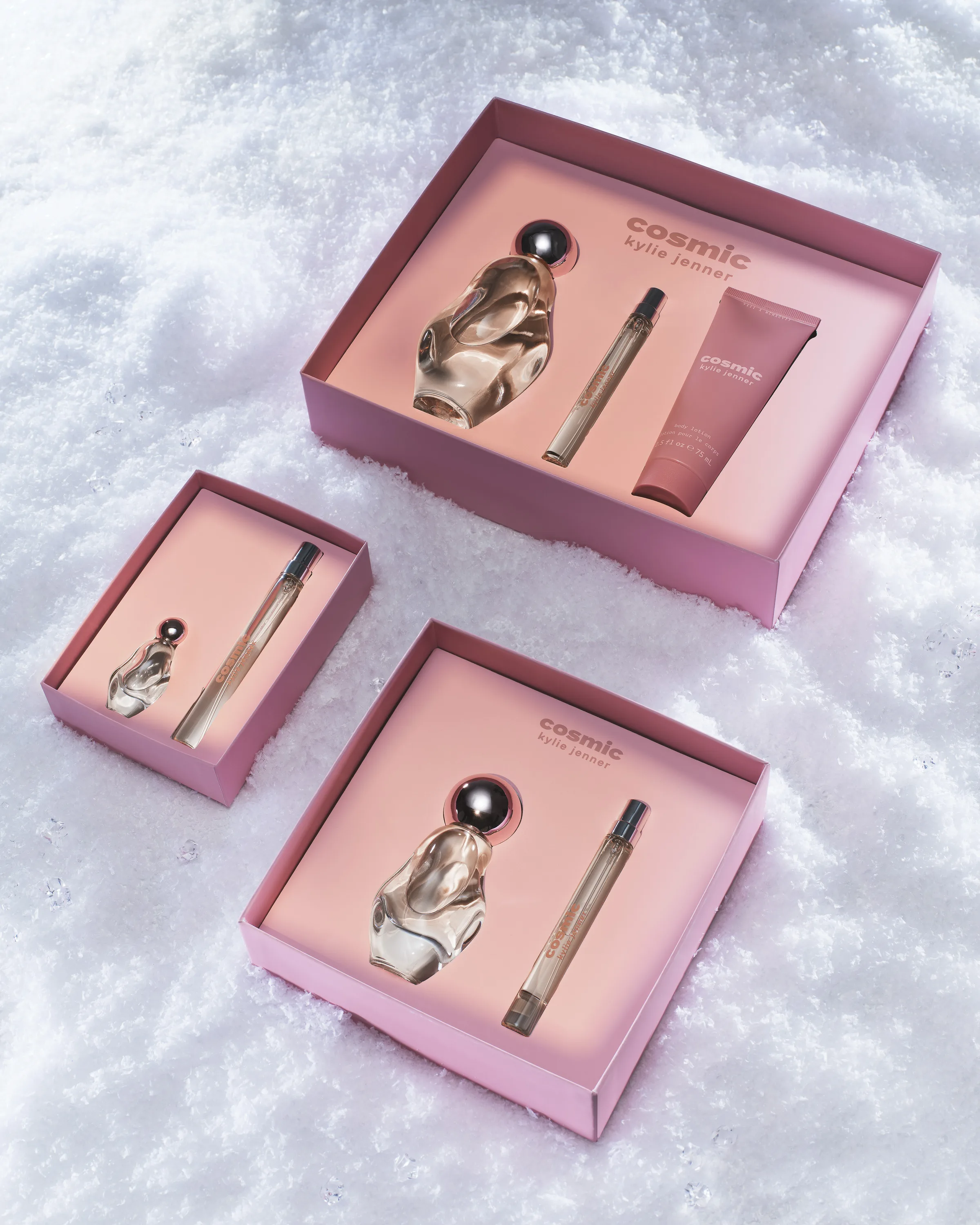 Three pink Cosmic Kylie Jenner fragrance gift sets with perfume bottles and rollerballs nestled in snow, for Kylie Cosmetics.