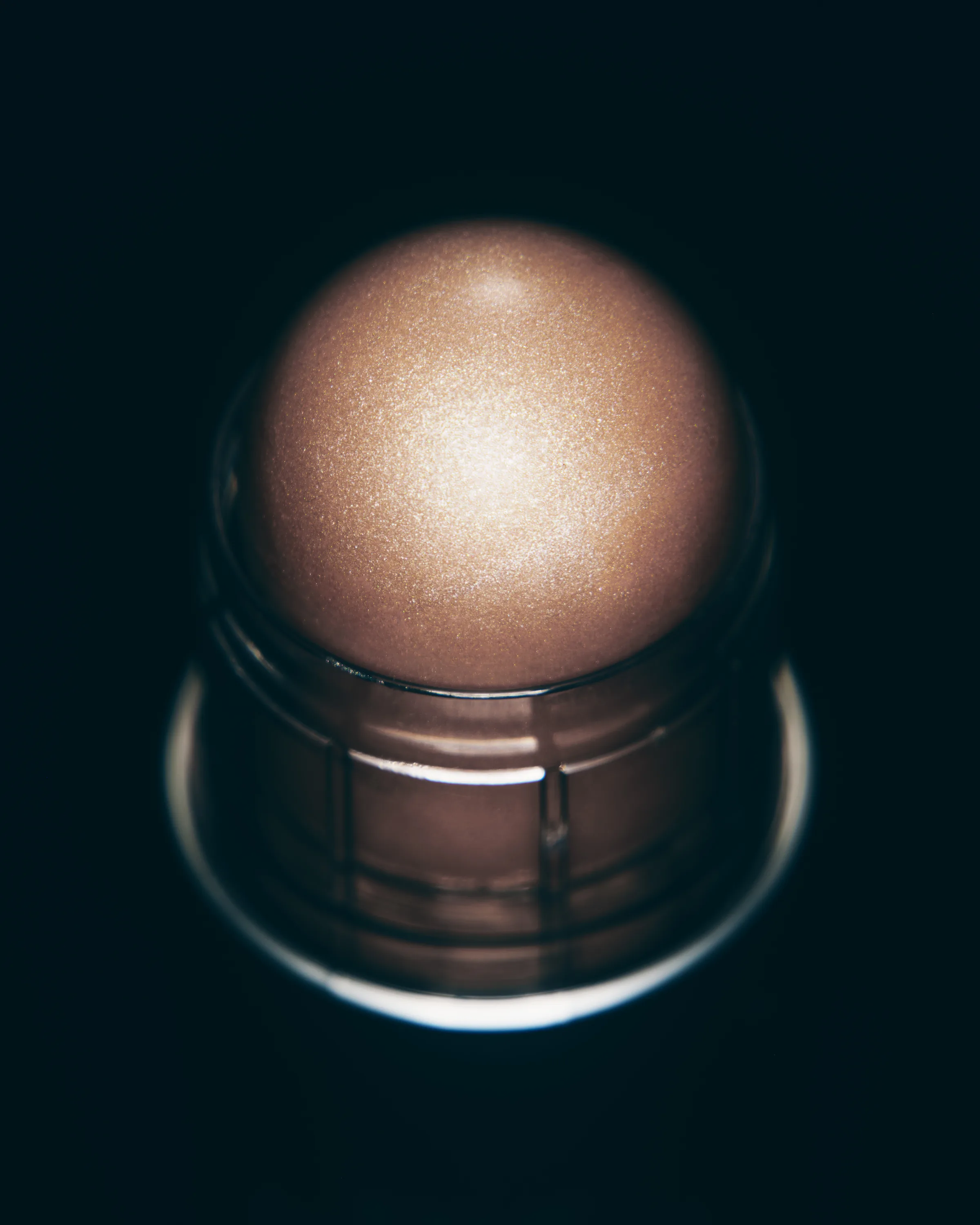 Close-up of a shimmering bronze dewy balm stick in shade Lunar Sky against a black background, for Kylie Cosmetics.