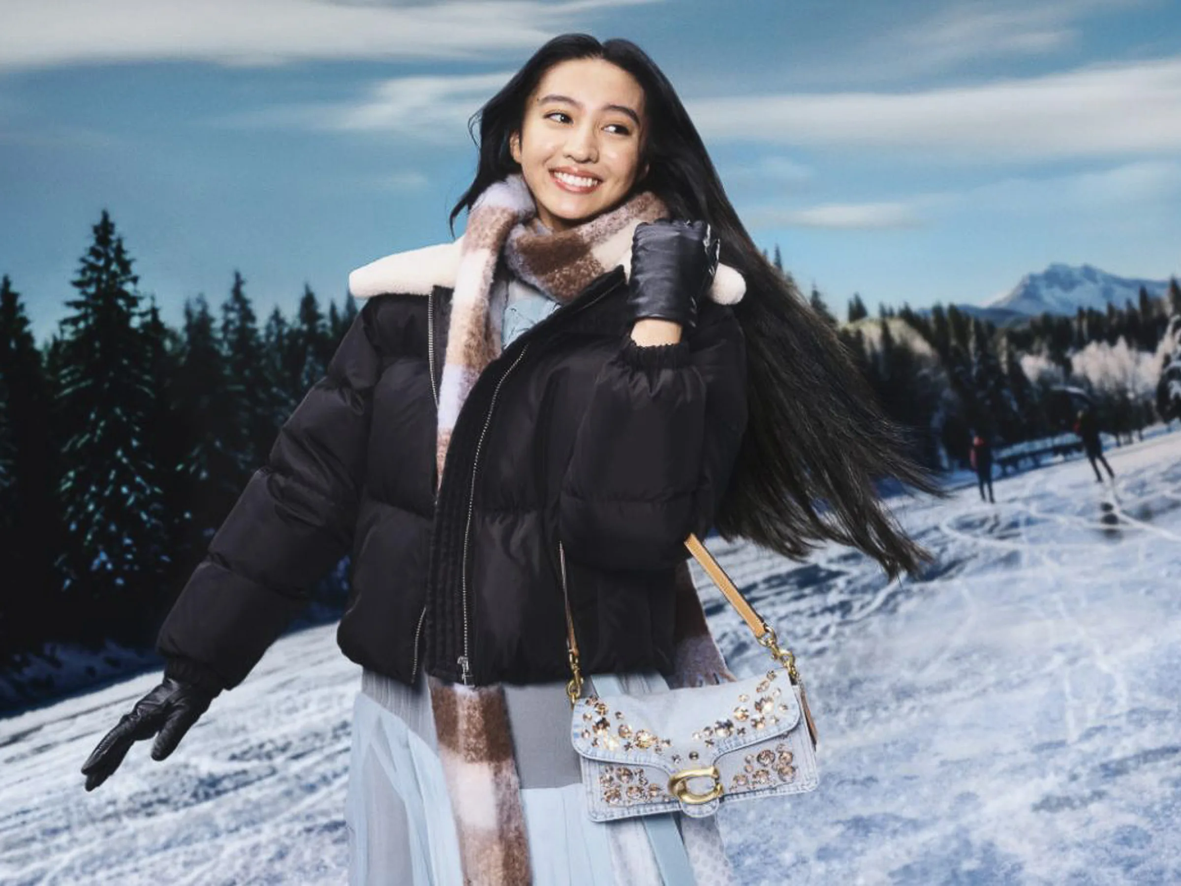 AI image of a smiling model in a black puffer jacket and plaid scarf with an embellished bag on a snowy rink, for Coach.