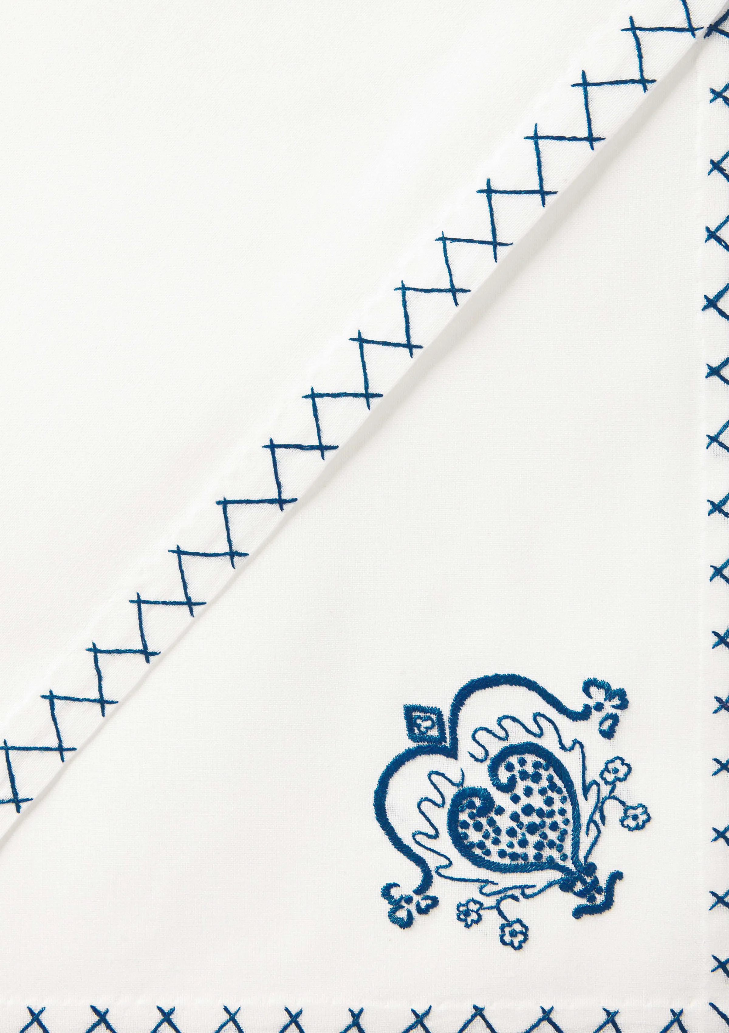 White cotton napkin folded diagonally with blue cross-stitch edging and an embroidered blue heart motif, for Rhode.