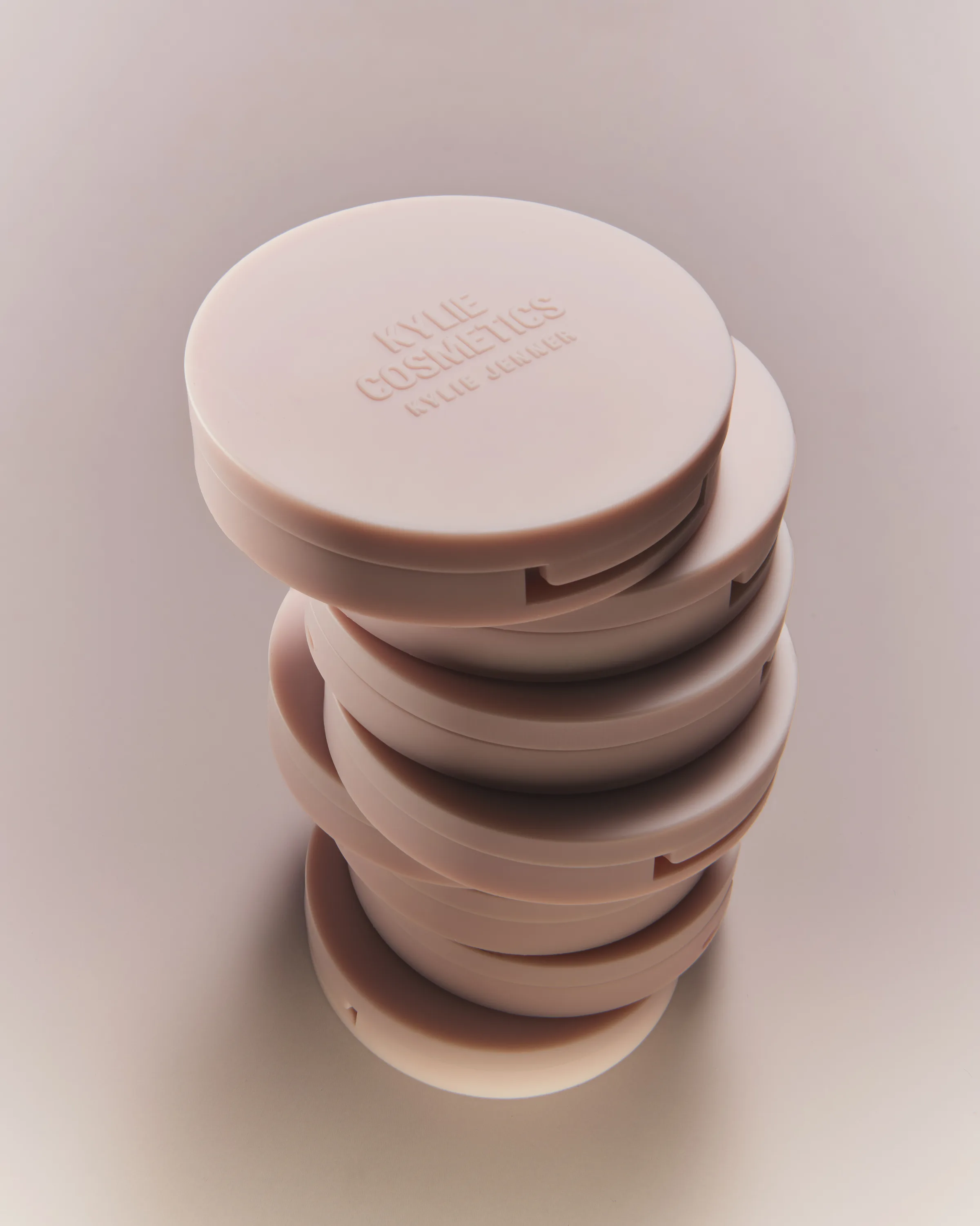 Stack of pale pink blush compacts with embossed logo lids on a soft pink-grey background, for Kylie Cosmetics.