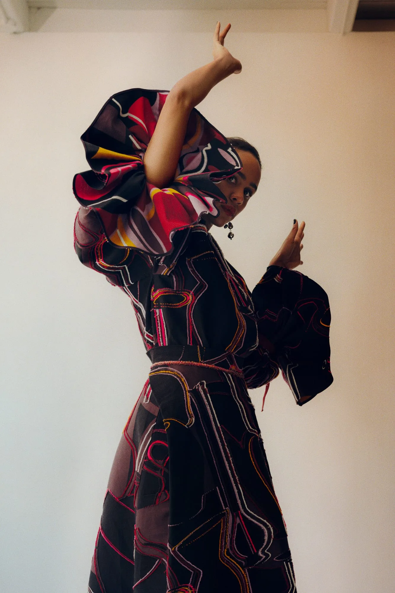 Model posing in a black gown with red and gold abstract embroidery and an oversized ruffled collar, for The Last Magazine.