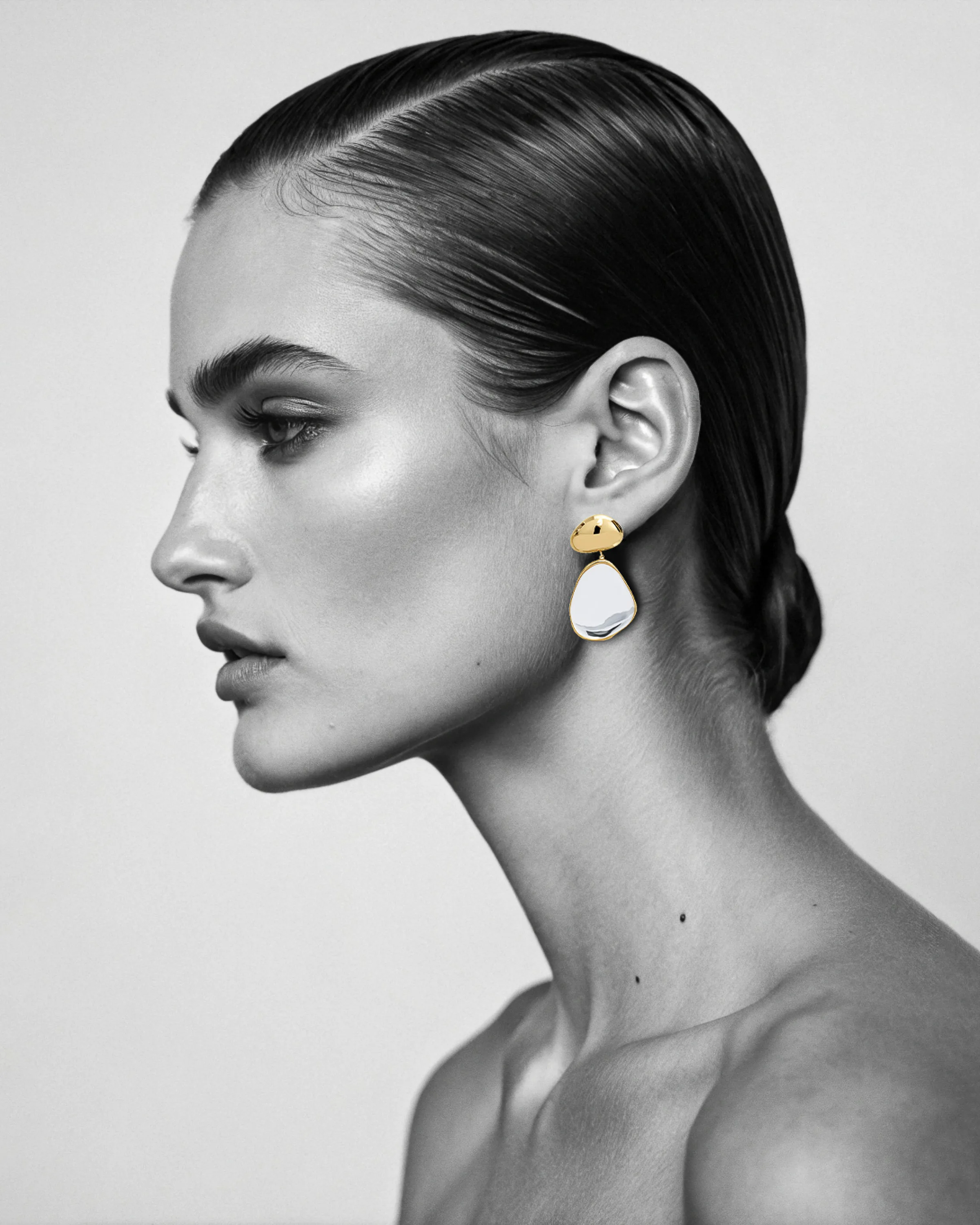 AI image of a model in black-and-white profile, slicked hair, wearing a gold and white drop earring. Alaïa AI Concept.