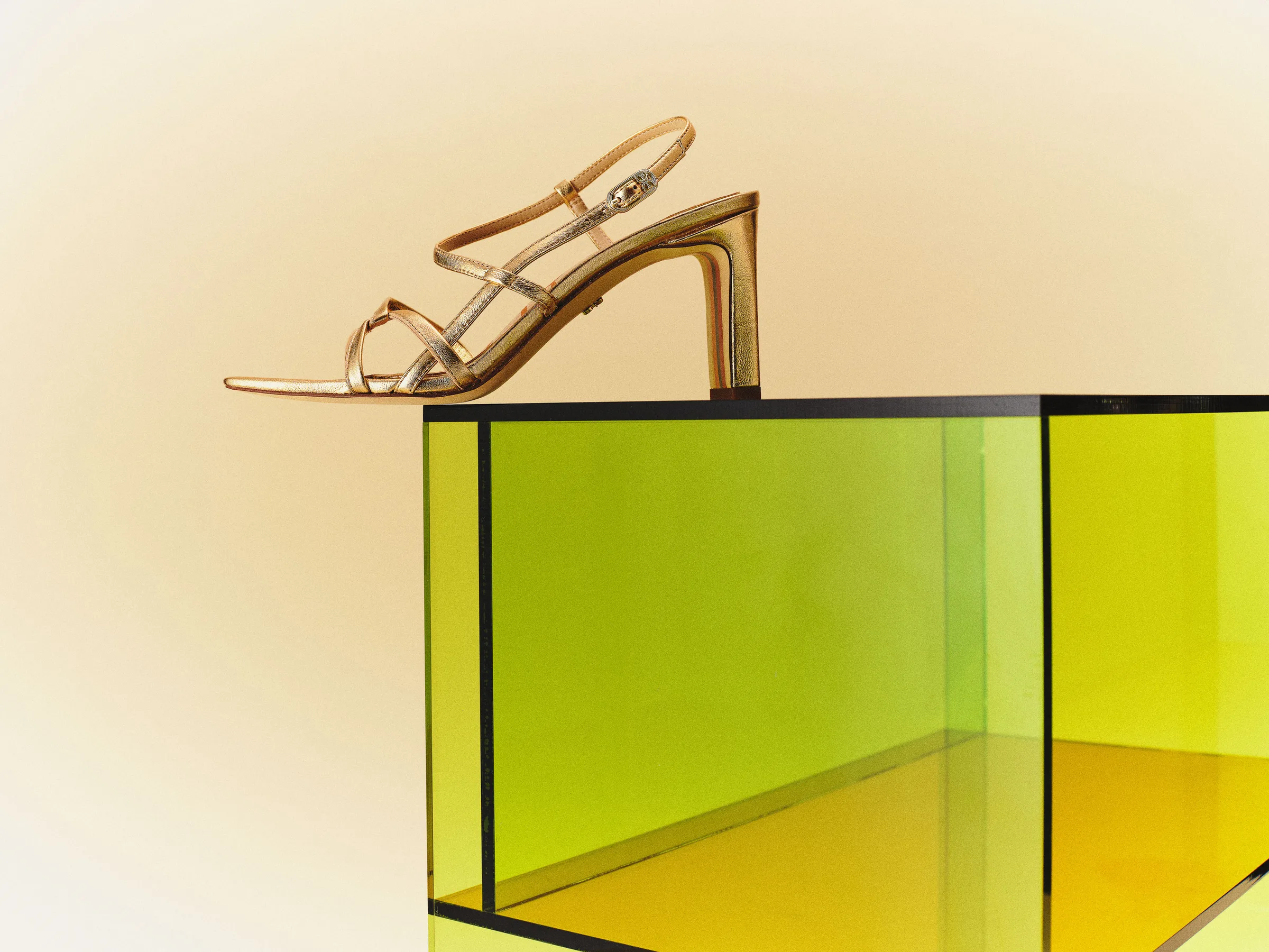 Gold metallic strappy heeled sandal perched on a lime green acrylic cube against a warm gradient backdrop, for Sam Edelman.