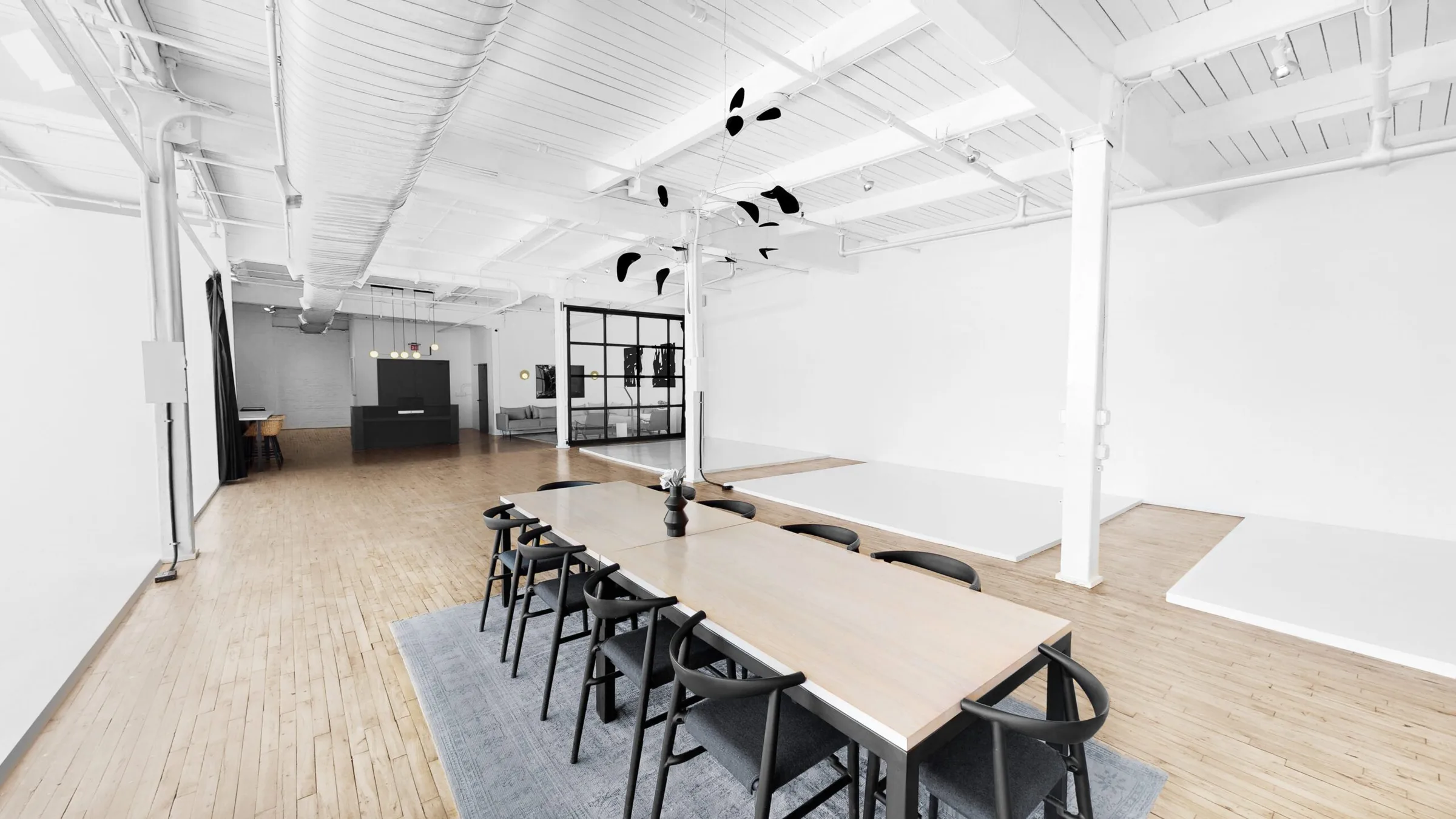 Studio 1 with a long wooden table and black chairs on a grey rug, white beams, cyc walls and hardwood floors at Slate Studios.