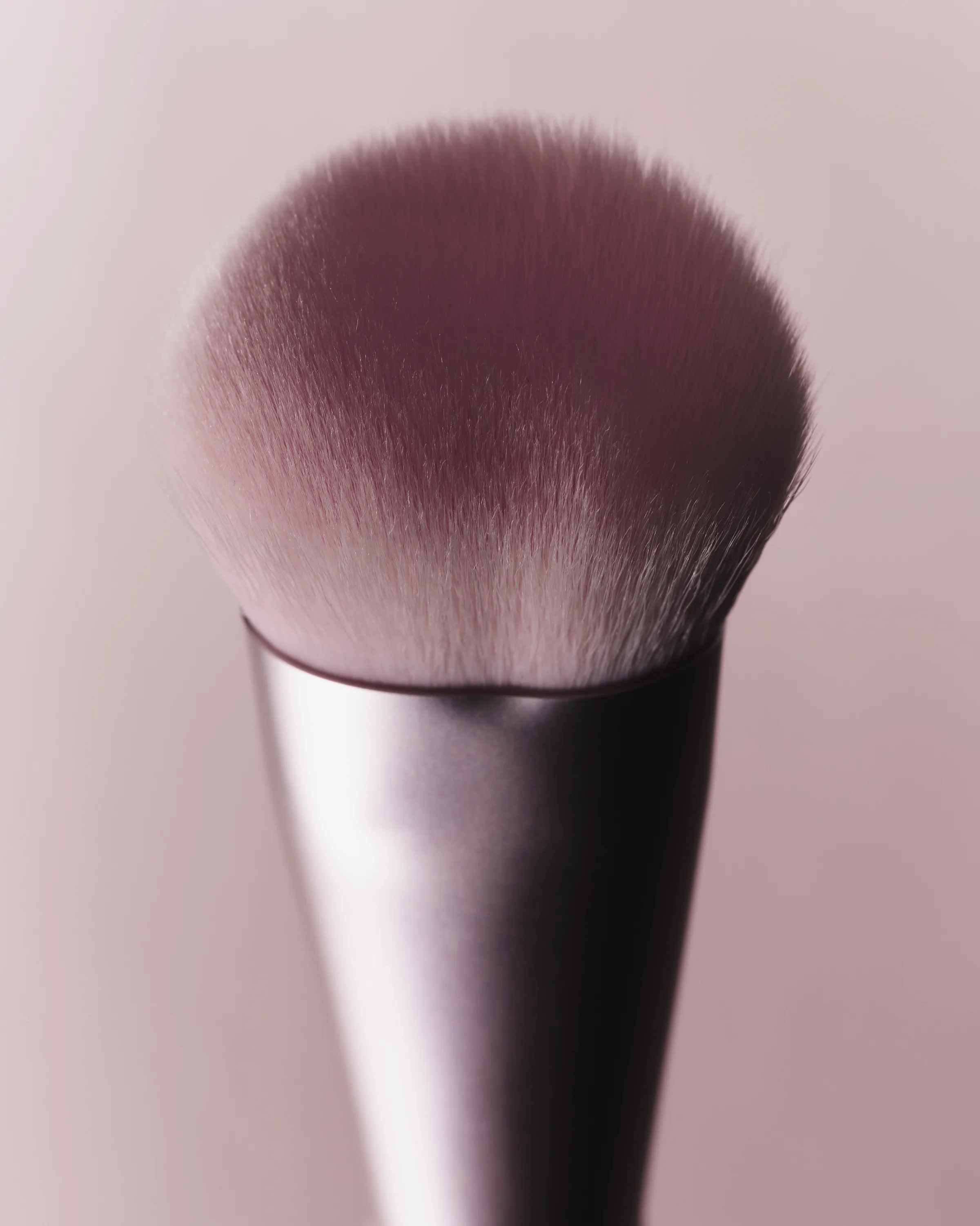 Close-up of a domed pink makeup brush with a metallic mauve ferrule on a pale pink background, for Kylie Cosmetics.
