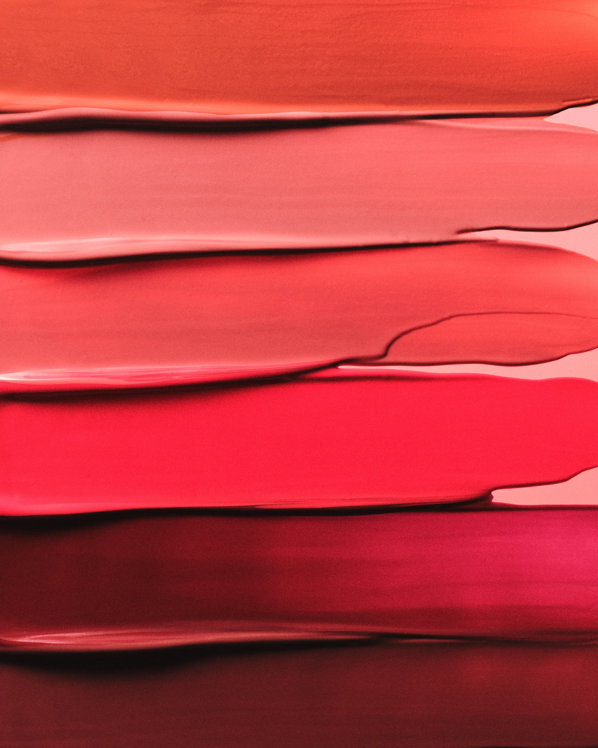 Smeared lipstick swatches in stacked bands from coral and pink to bright red and deep berry, for Kylie Cosmetics.