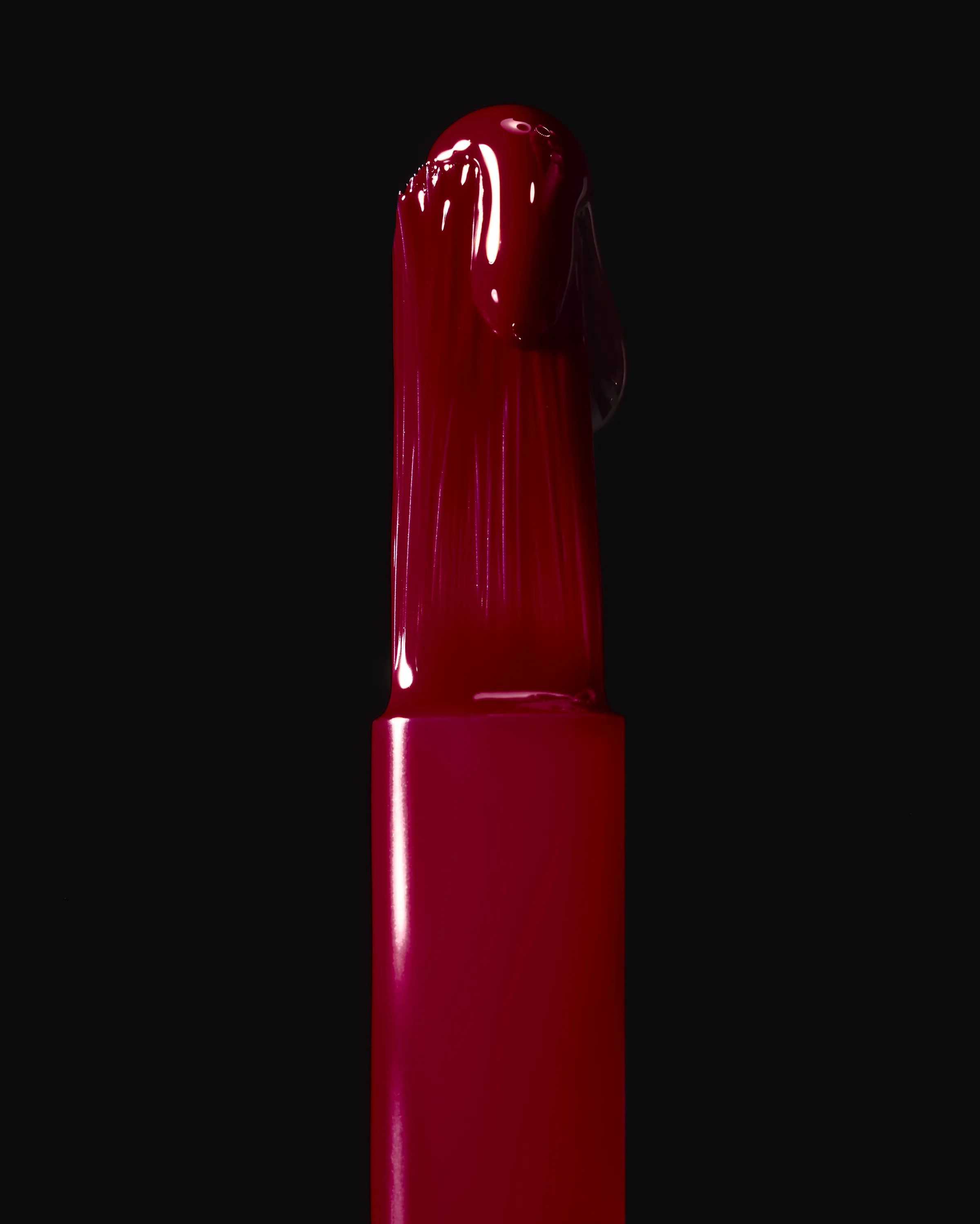 Close-up of a nail lacquer brush dripping glossy deep red polish against a black background, for Kylie Cosmetics.