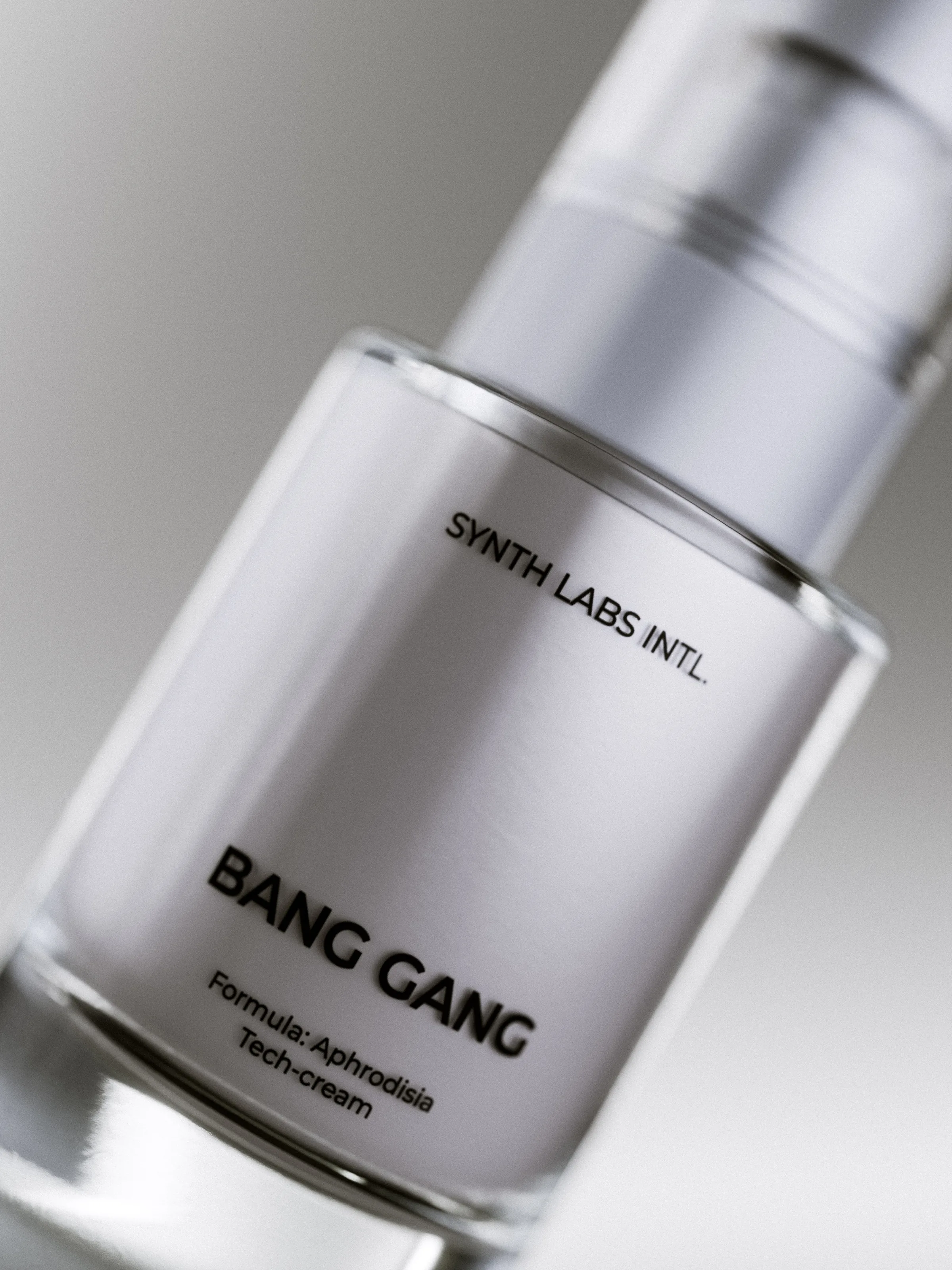 CGI render of a silver Bang Gang tech-cream pump bottle, tilted close-up on a grey background, for Synth Labs Intl.