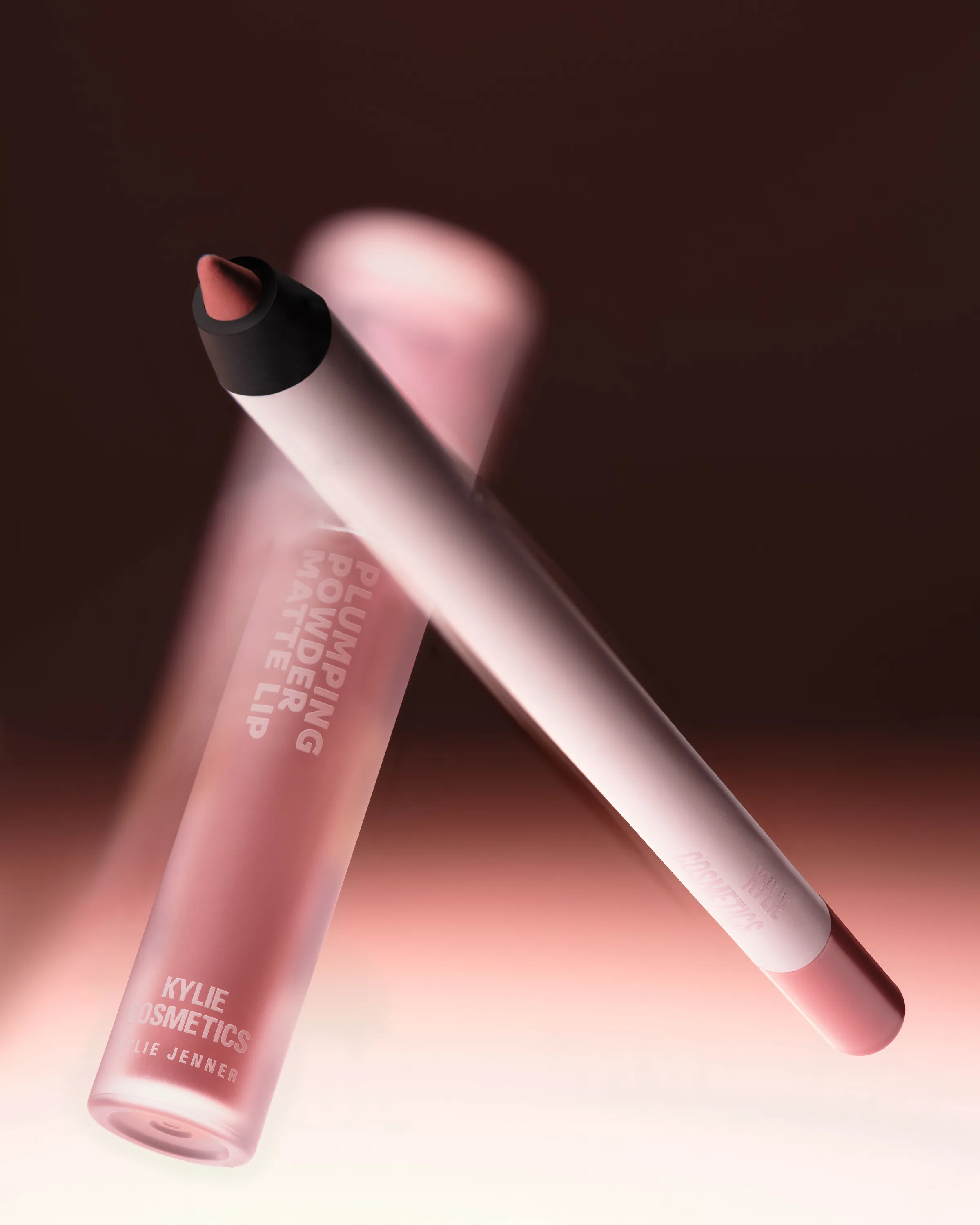 Pink Plumping Powder Matte Lip tube and lip liner crossing in motion blur on a dark backdrop, for Kylie Cosmetics.