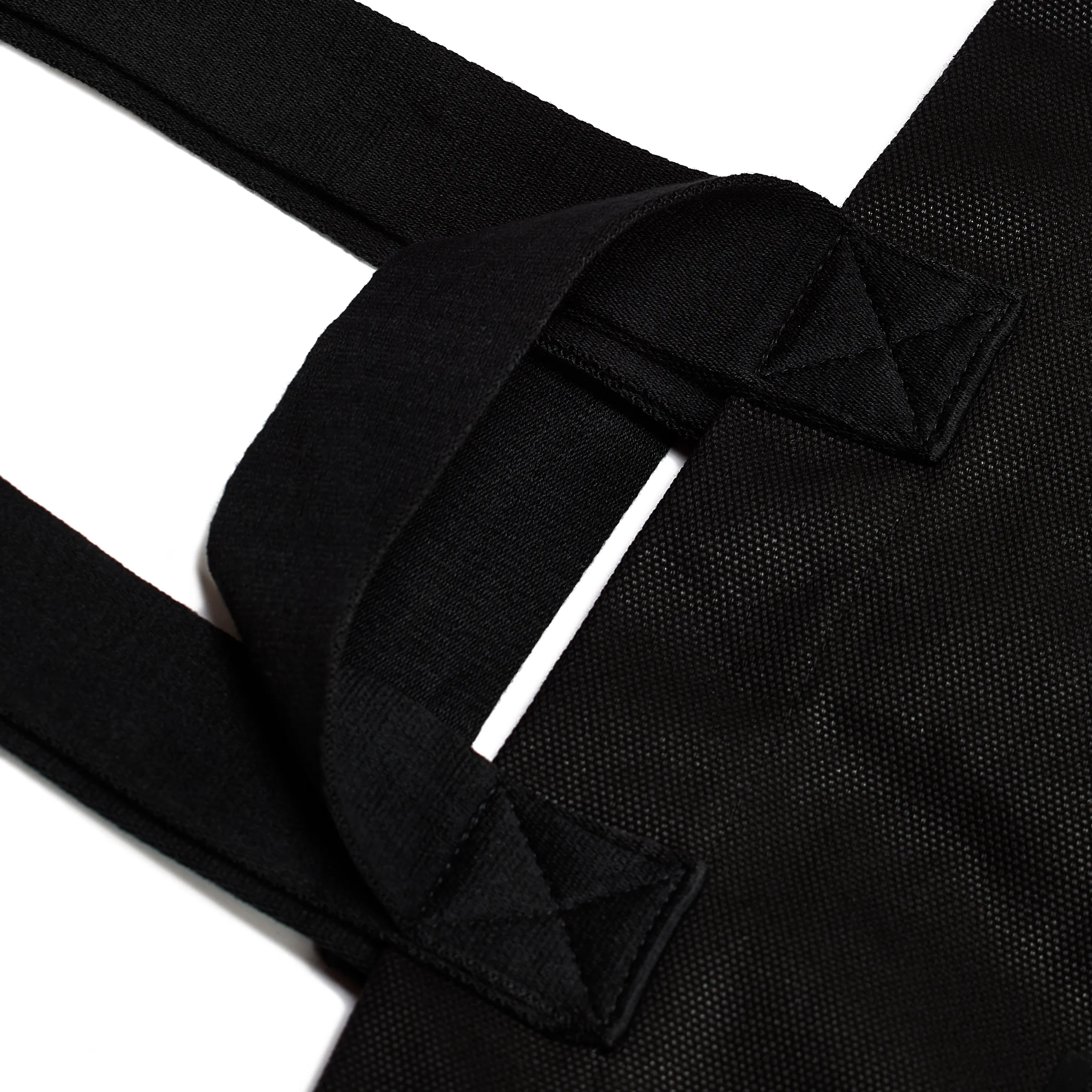 Close-up of a black canvas tote bag's strap handles with box-stitched seams on a white background, for Strata.