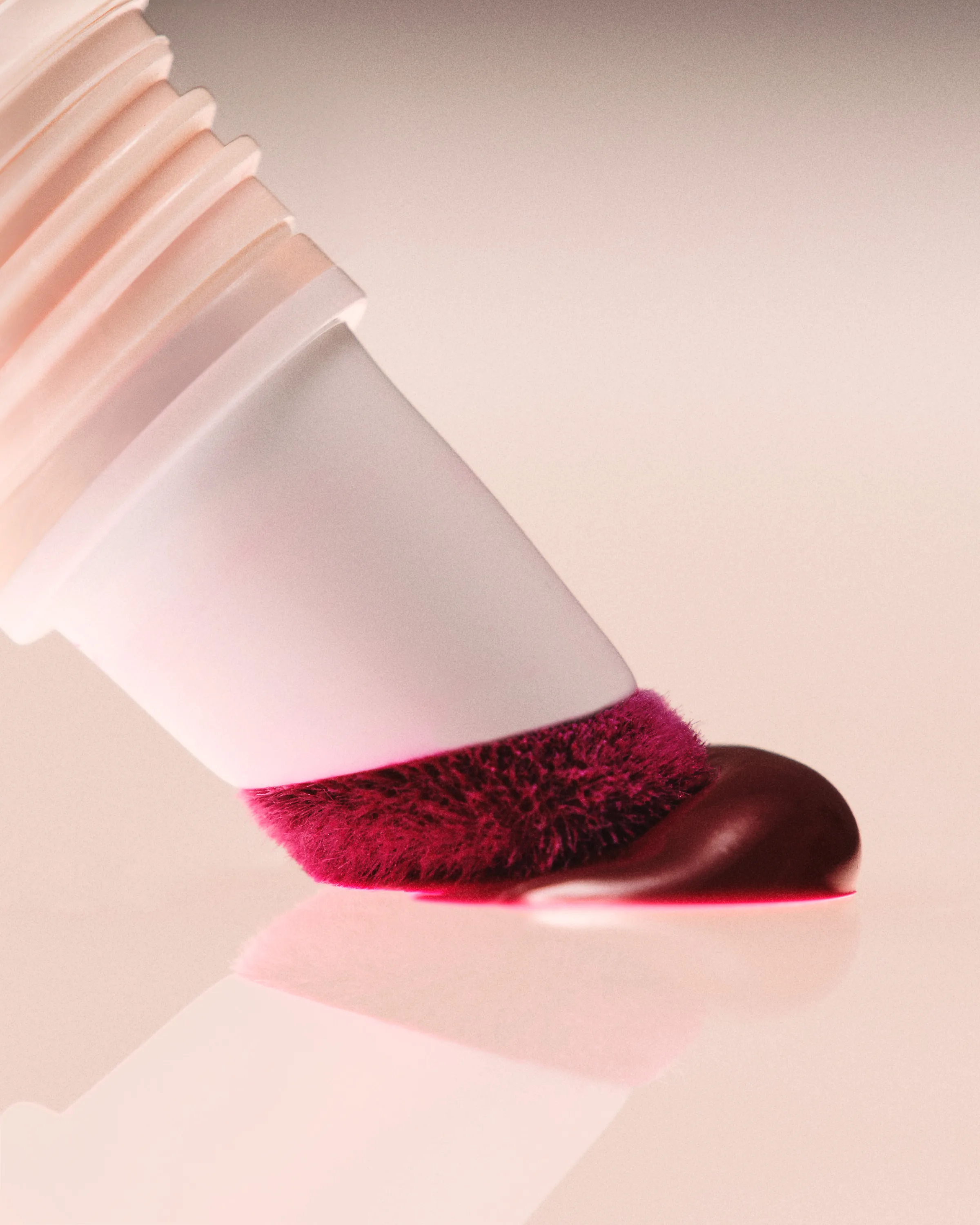 Close-up of a white cushion-tip applicator dispensing berry liquid blush onto a glossy pink surface, for Kylie Cosmetics.