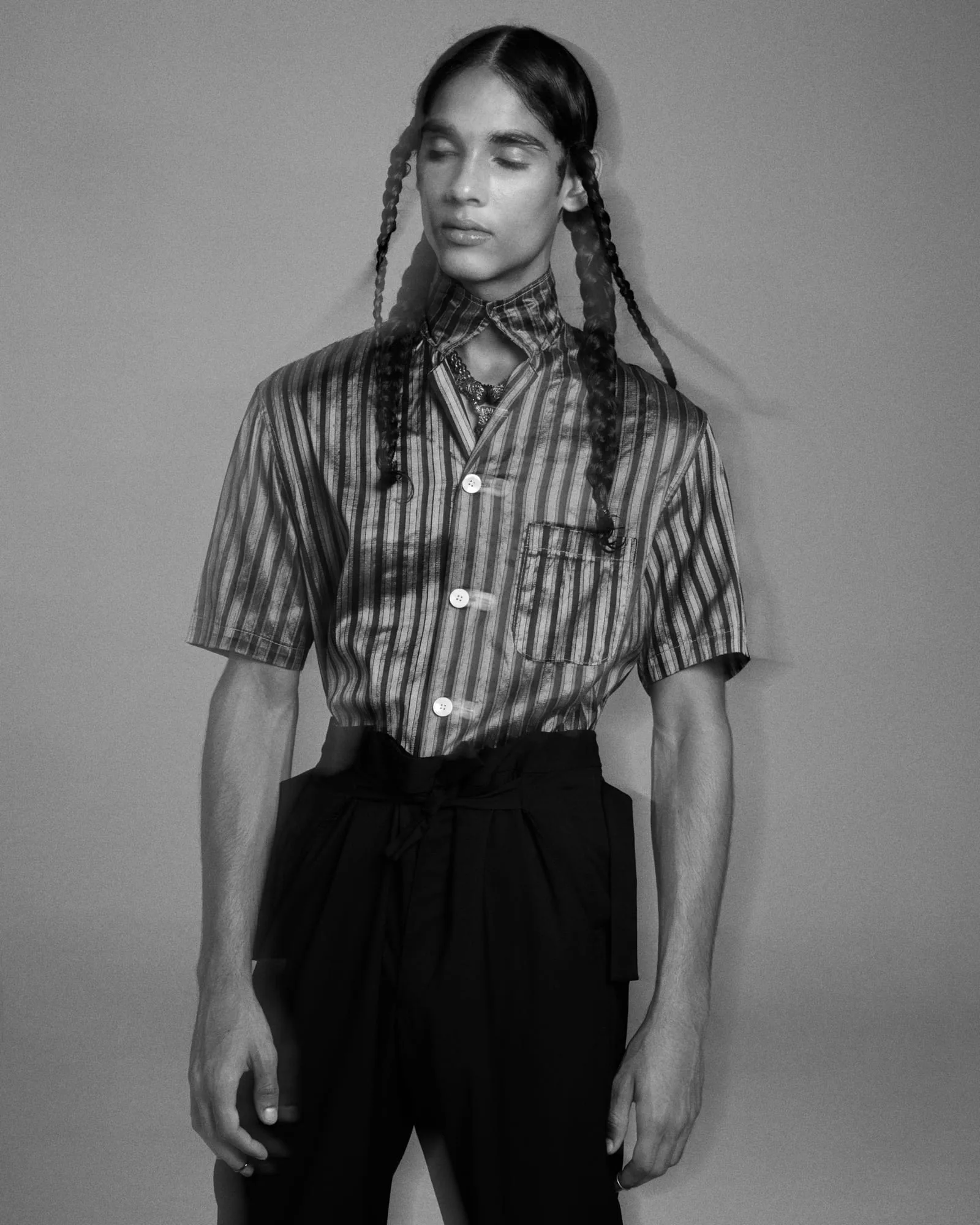Black and white editorial portrait of a model with long braids in a striped short-sleeve shirt and dark trousers, for The Last Magazine.