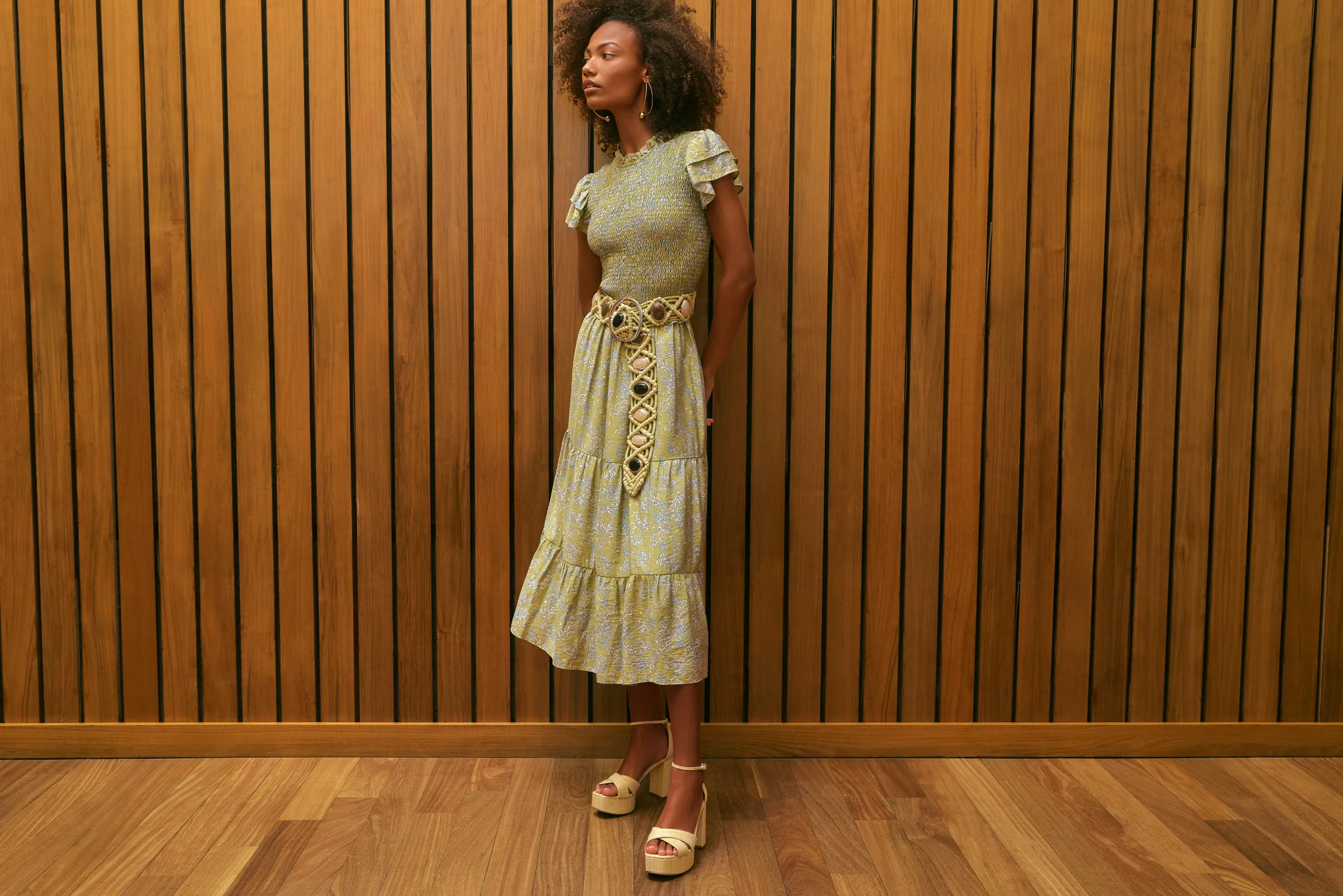 Model in a green smocked tiered midi dress and cream platform sandals against a wood-slat wall, for Sam Edelman.