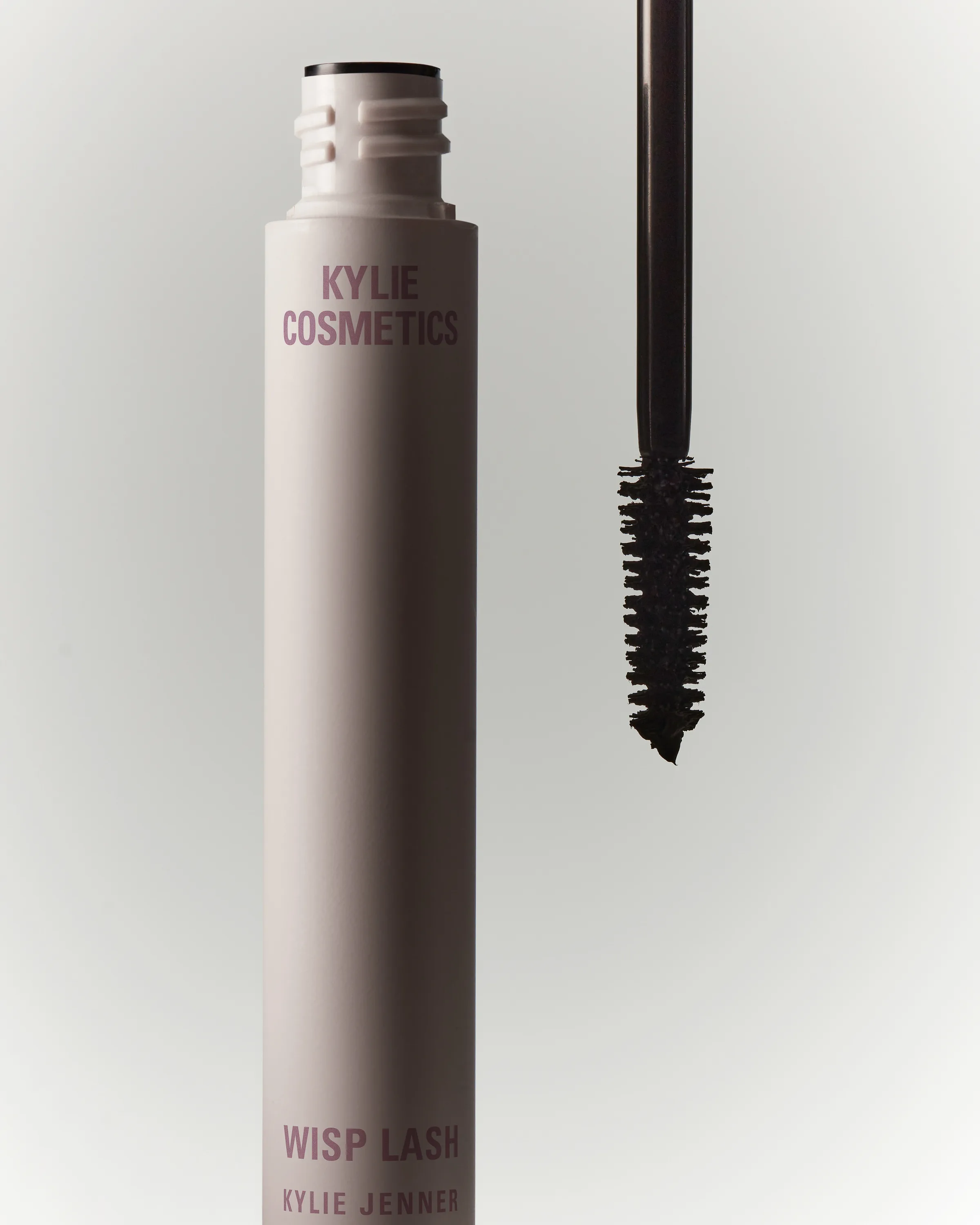 Open Wisp Lash mascara tube beside its black bristle wand on a soft grey background, for Kylie Cosmetics.
