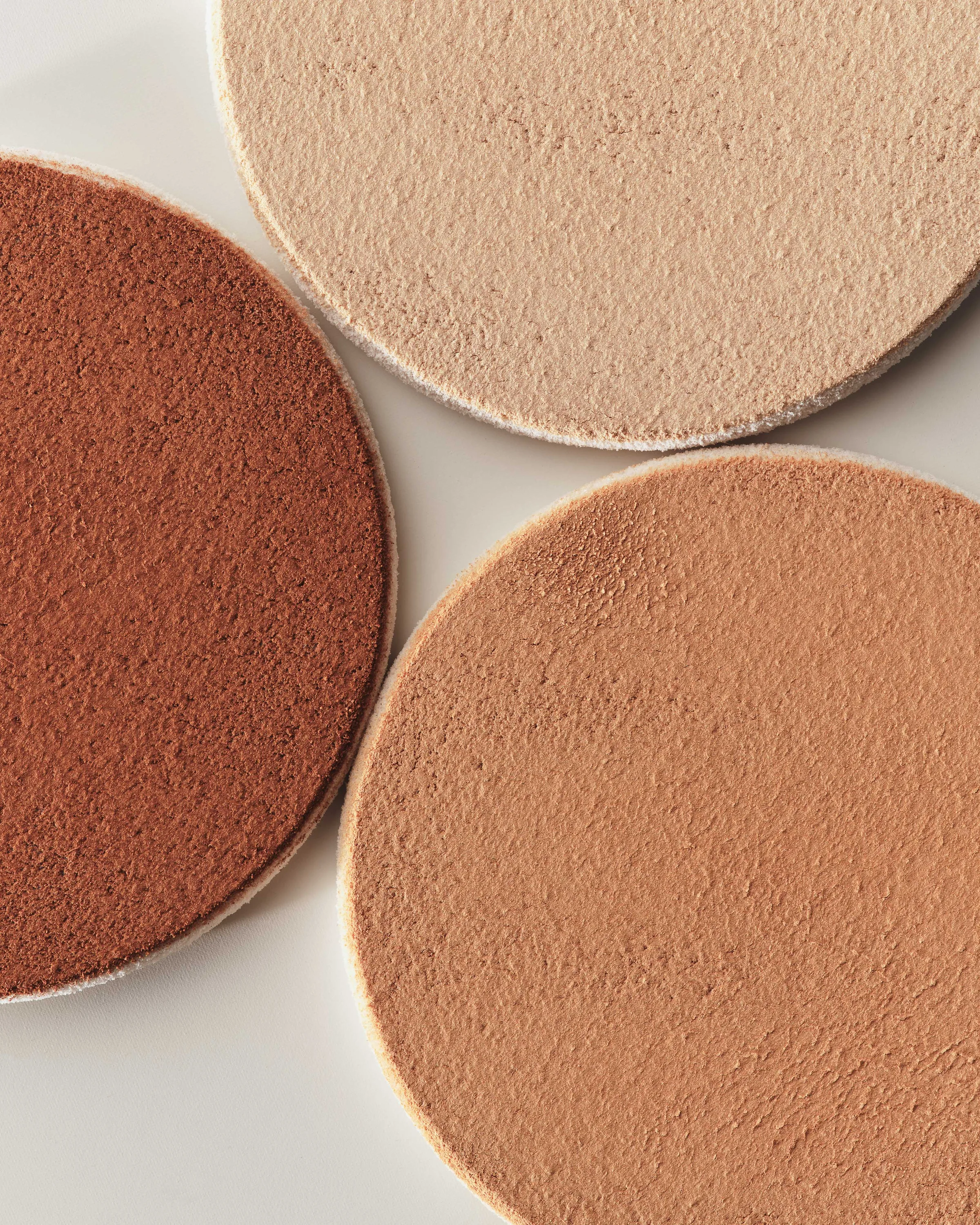 Close-up of three pressed powder foundation discs in light, tan and deep brown shades on white, for Kylie Cosmetics.