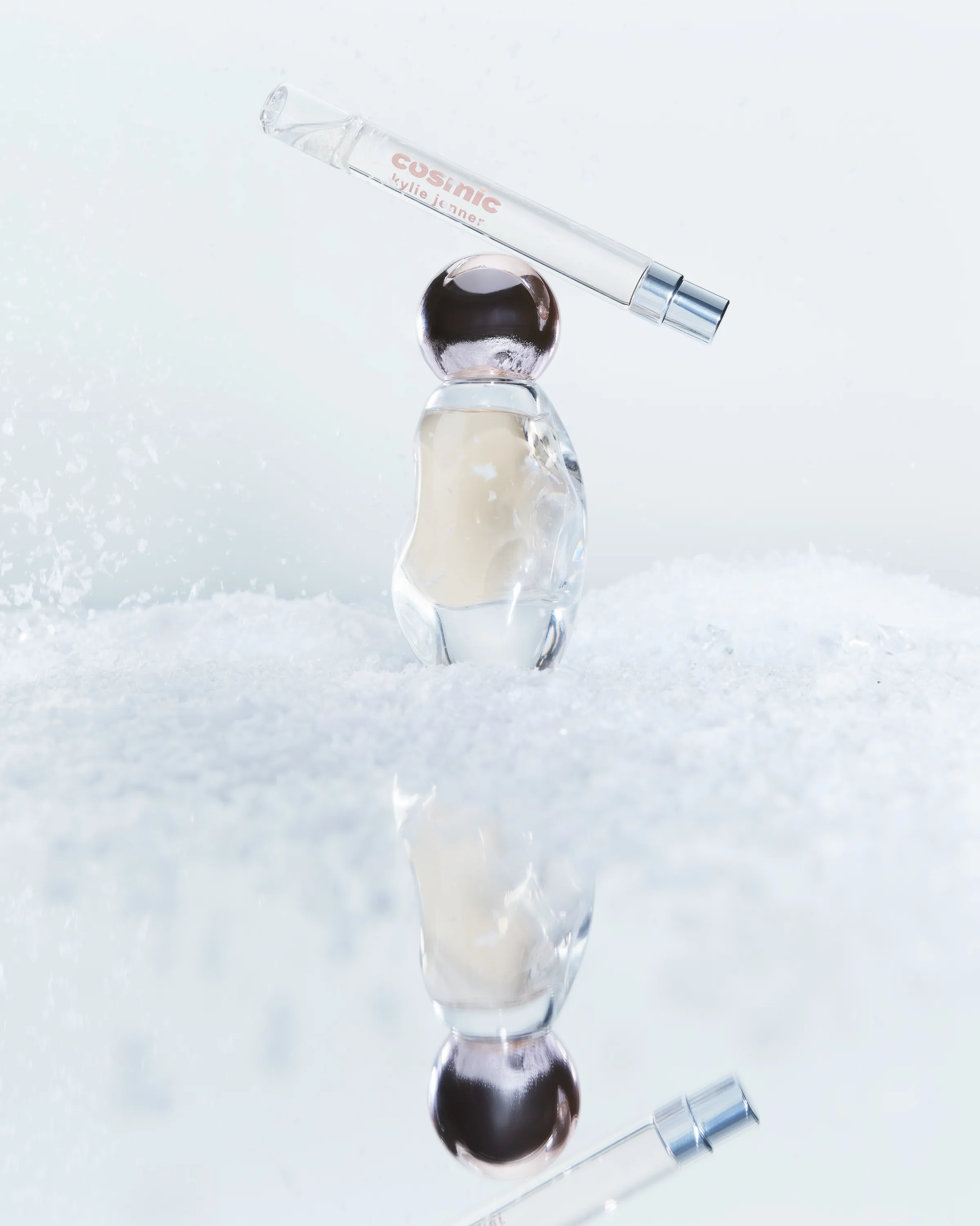Cosmic perfume bottle balancing a pen spray on top, set in snow with a mirrored reflection, for Kylie Cosmetics.