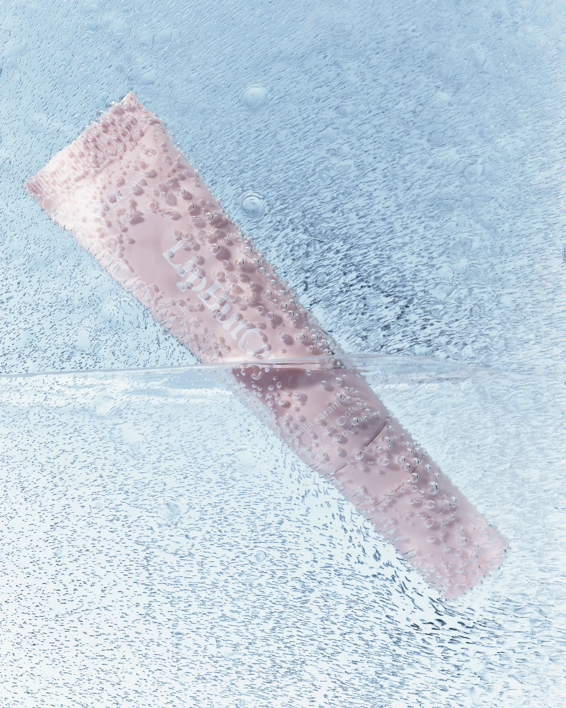Pink lip product tube frozen in clear ice with trapped bubbles on a pale blue background, for Kylie Cosmetics.