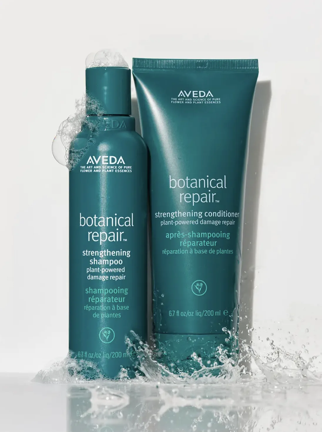 Teal Botanical Repair shampoo bottle and conditioner tube in a water splash with foam on a white background, for Aveda.