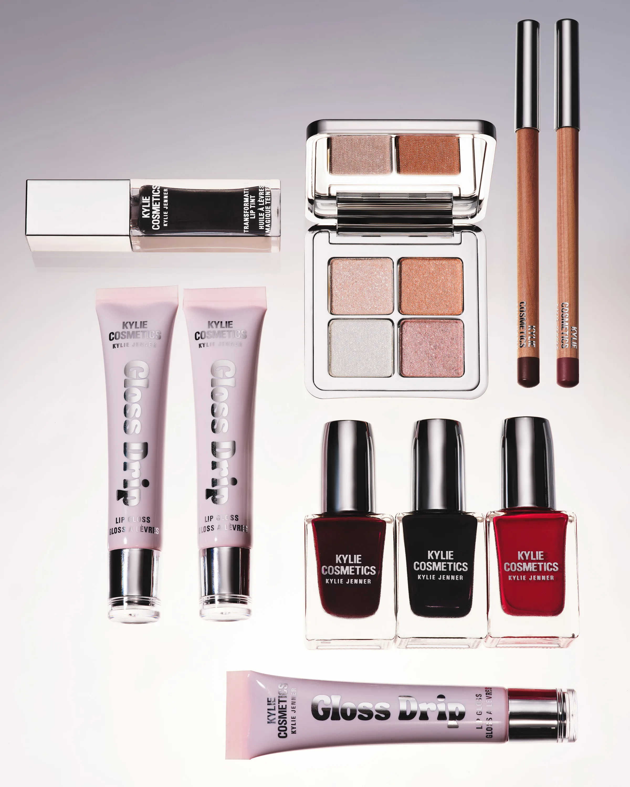 Gloss Drip tubes, eyeshadow palette, lip liners and dark nail polishes arranged on a pale grey backdrop, for Kylie Cosmetics.