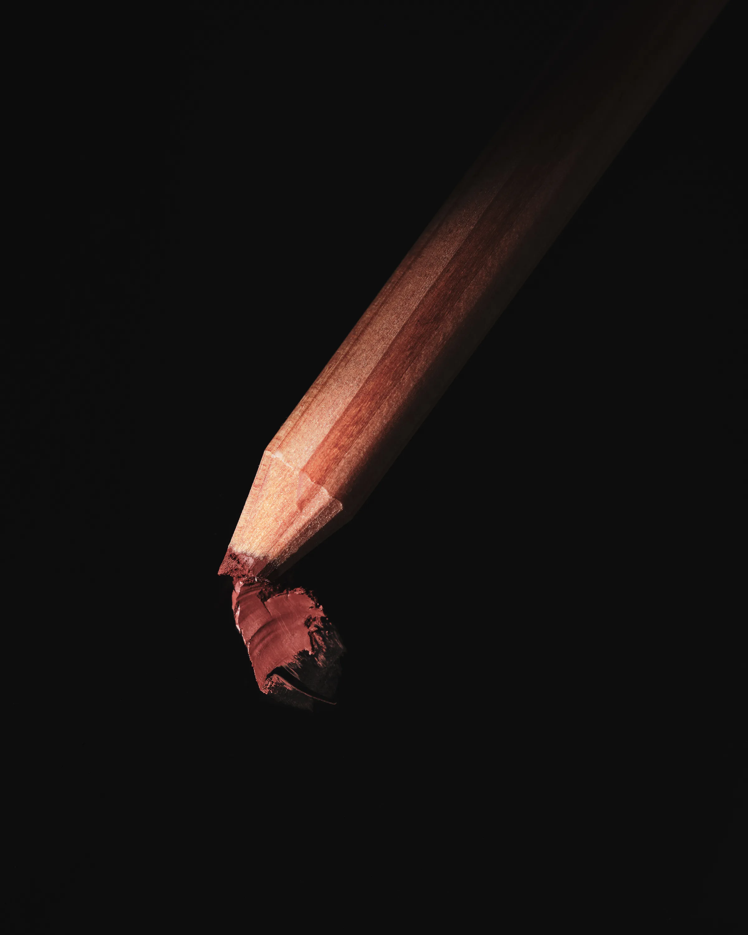 Wooden lip liner pencil with a smudged maple-red tip against a black background, for Kylie Cosmetics.