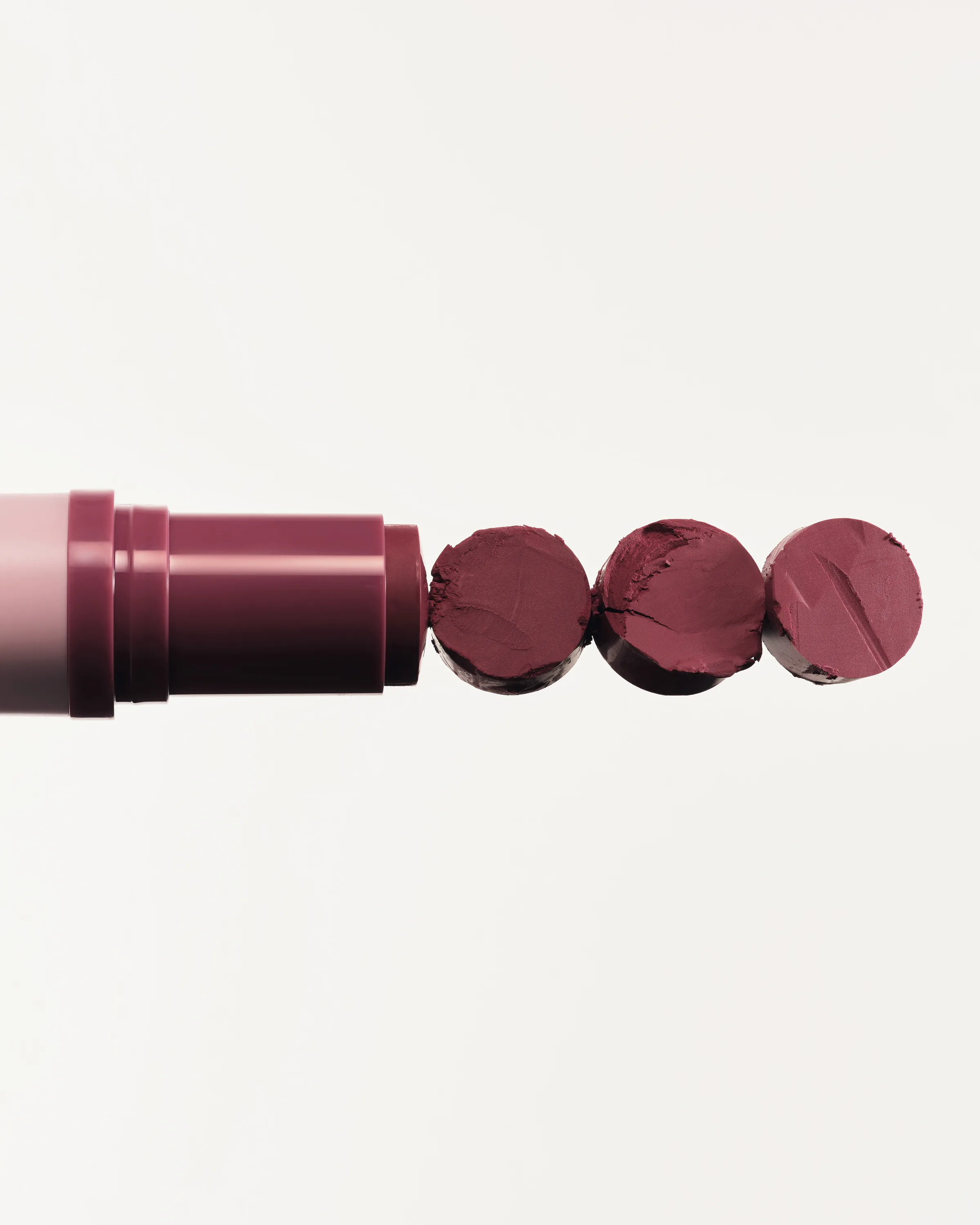 Berry lipstick tube with its bullet sliced into three discs, shot on an off-white background, for Kylie Cosmetics.