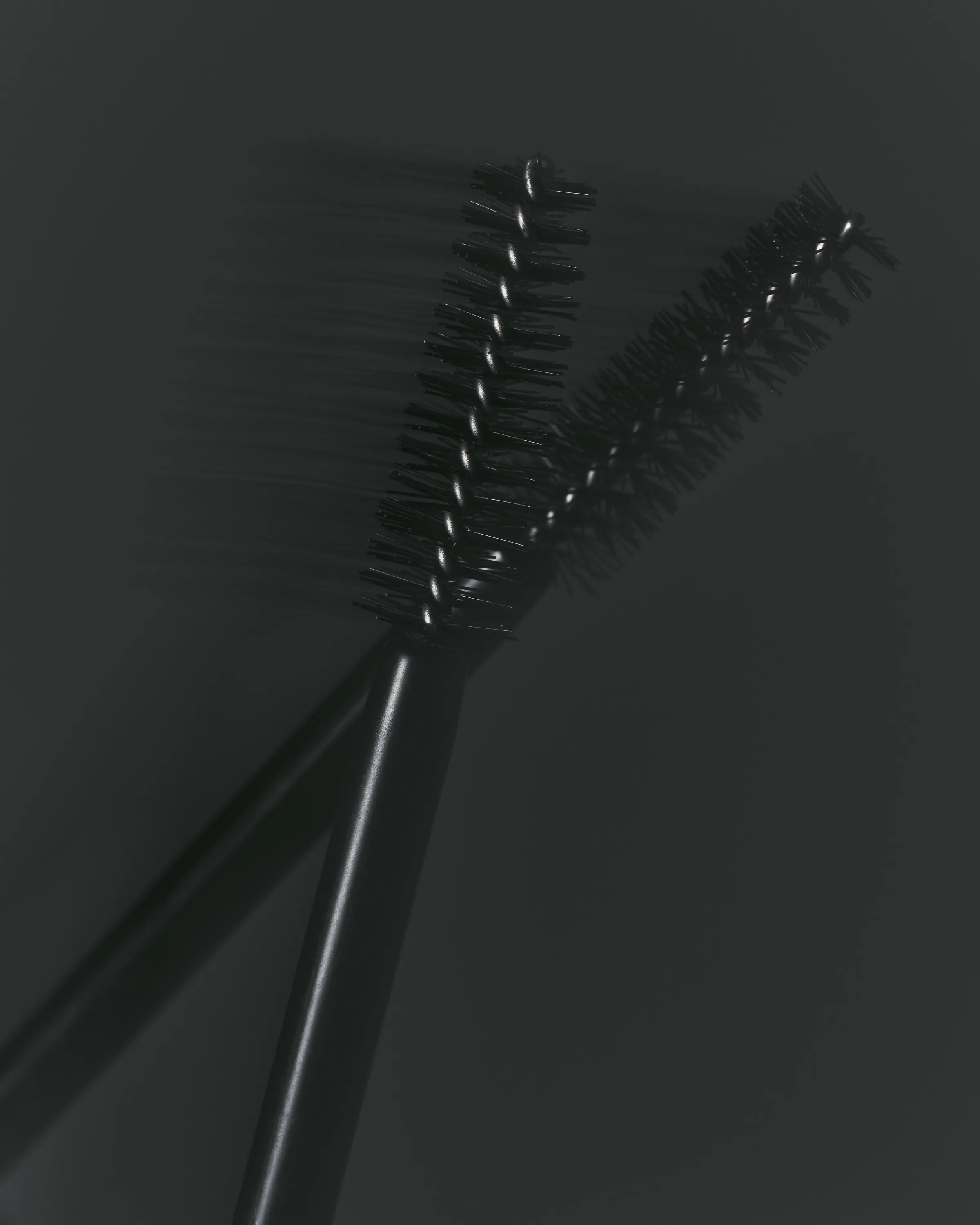 Two black mascara wands crossed against a dark grey background, one blurred in motion, for Kylie Cosmetics.
