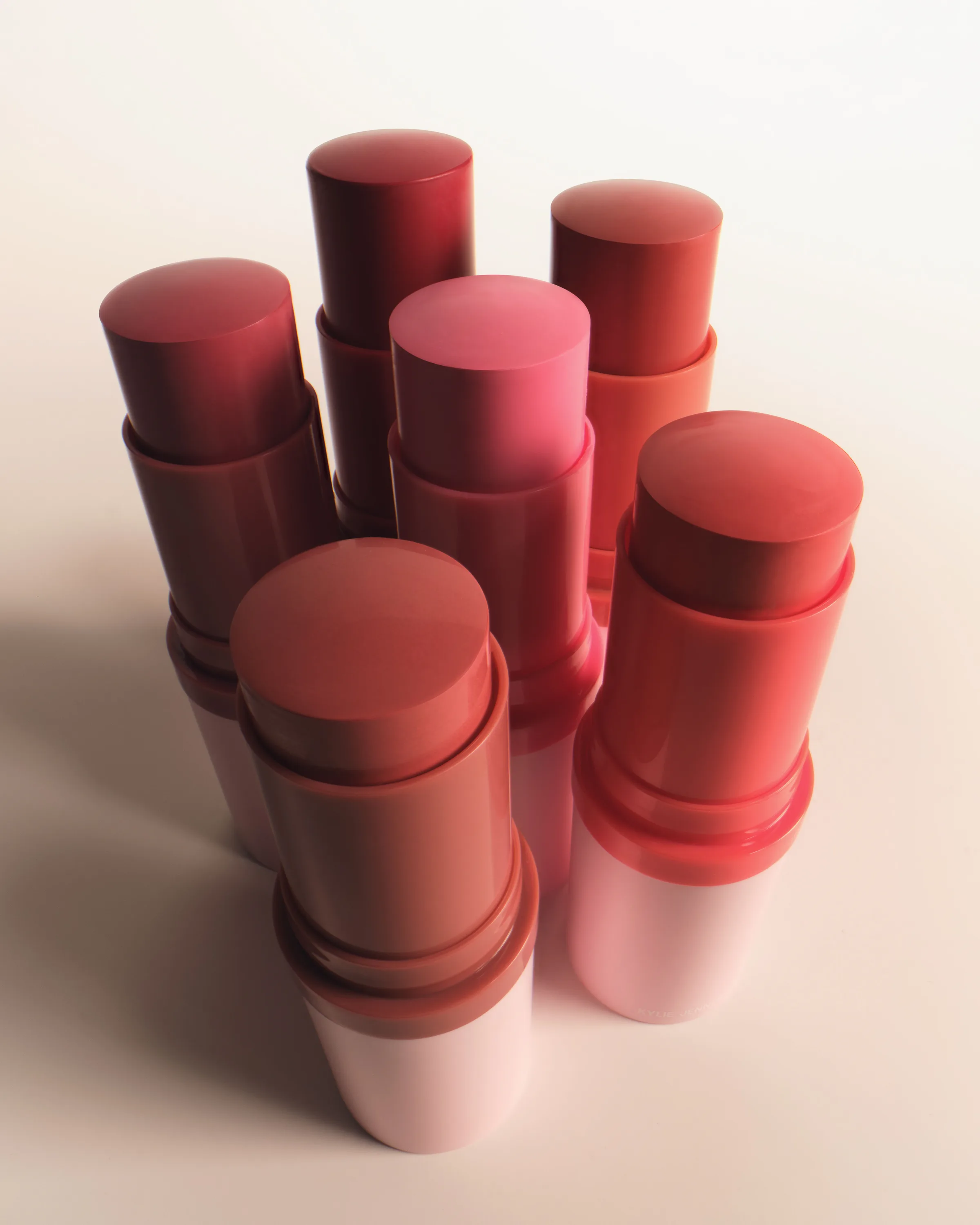 Six uncapped blush sticks in rose, coral and berry shades standing together on a soft white surface, for Kylie Cosmetics.