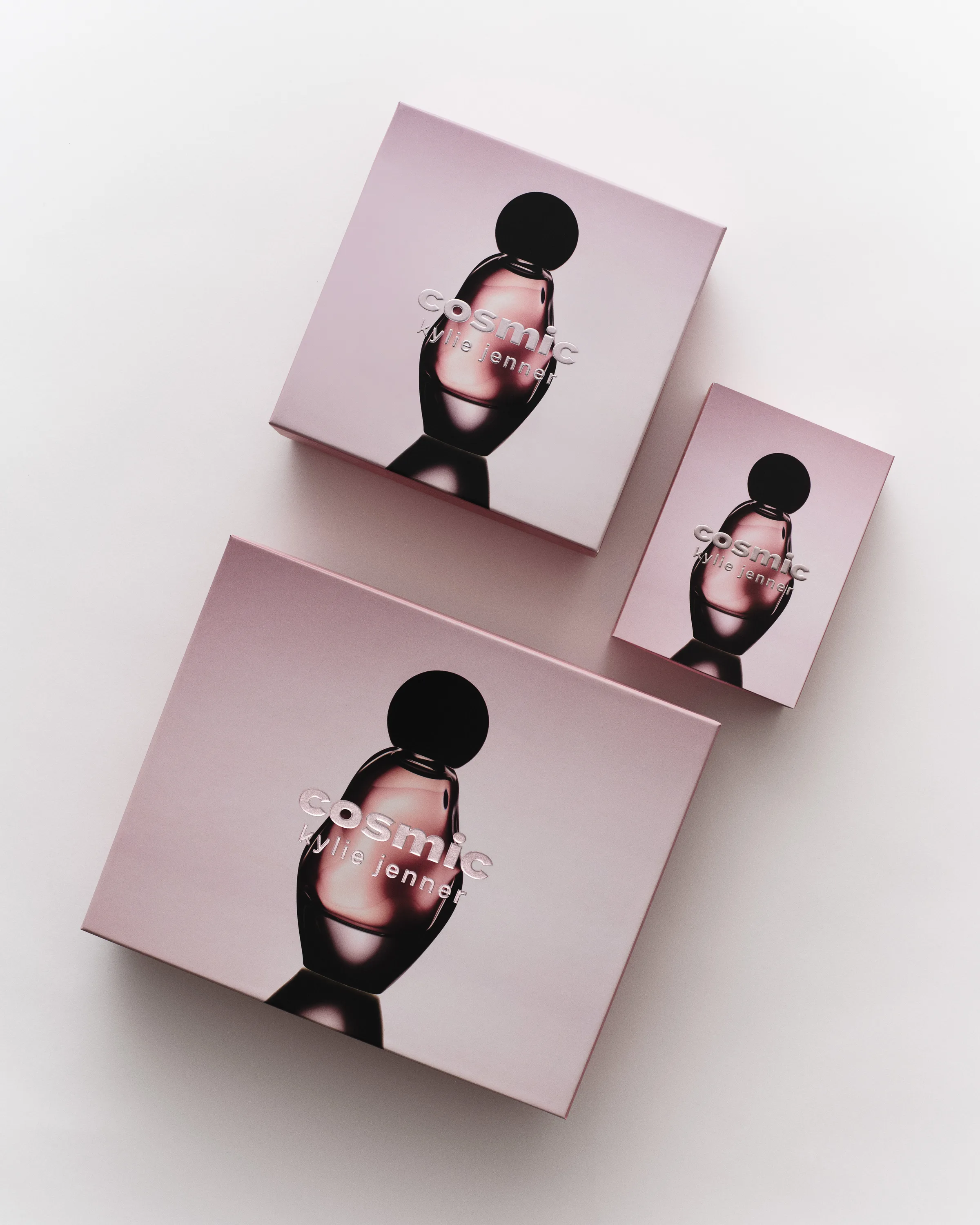 Three pink Cosmic Kylie Jenner fragrance gift boxes arranged flat lay on a white surface, for Kylie Cosmetics.