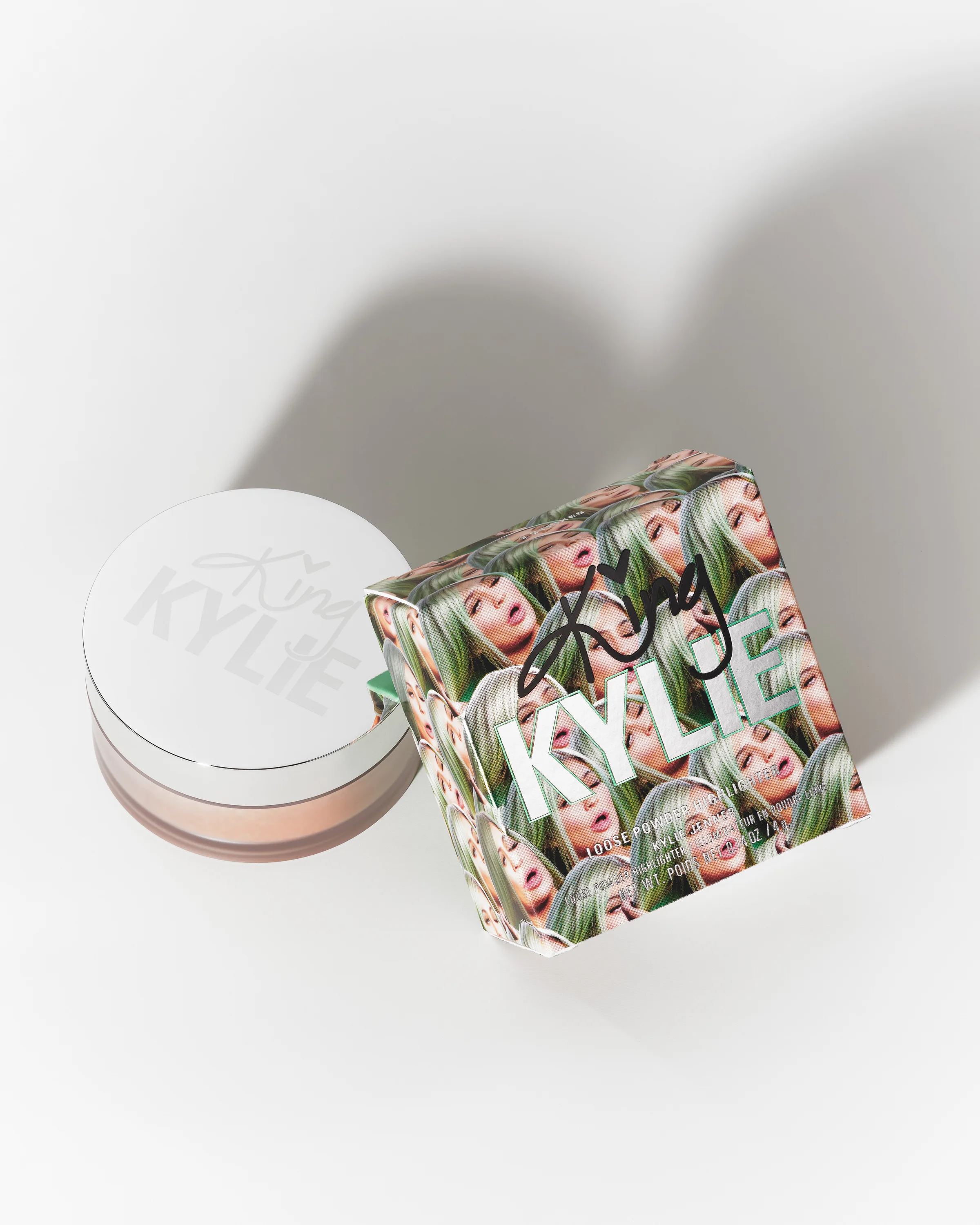 Loose powder highlighter jar beside its green King Kylie face-print box on white with a soft shadow, for Kylie Cosmetics.