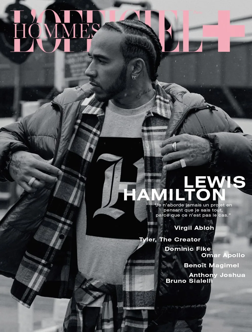 Black and white magazine cover of Lewis Hamilton in a puffer jacket and plaid shirt on a street, for L'Officiel Hommes.