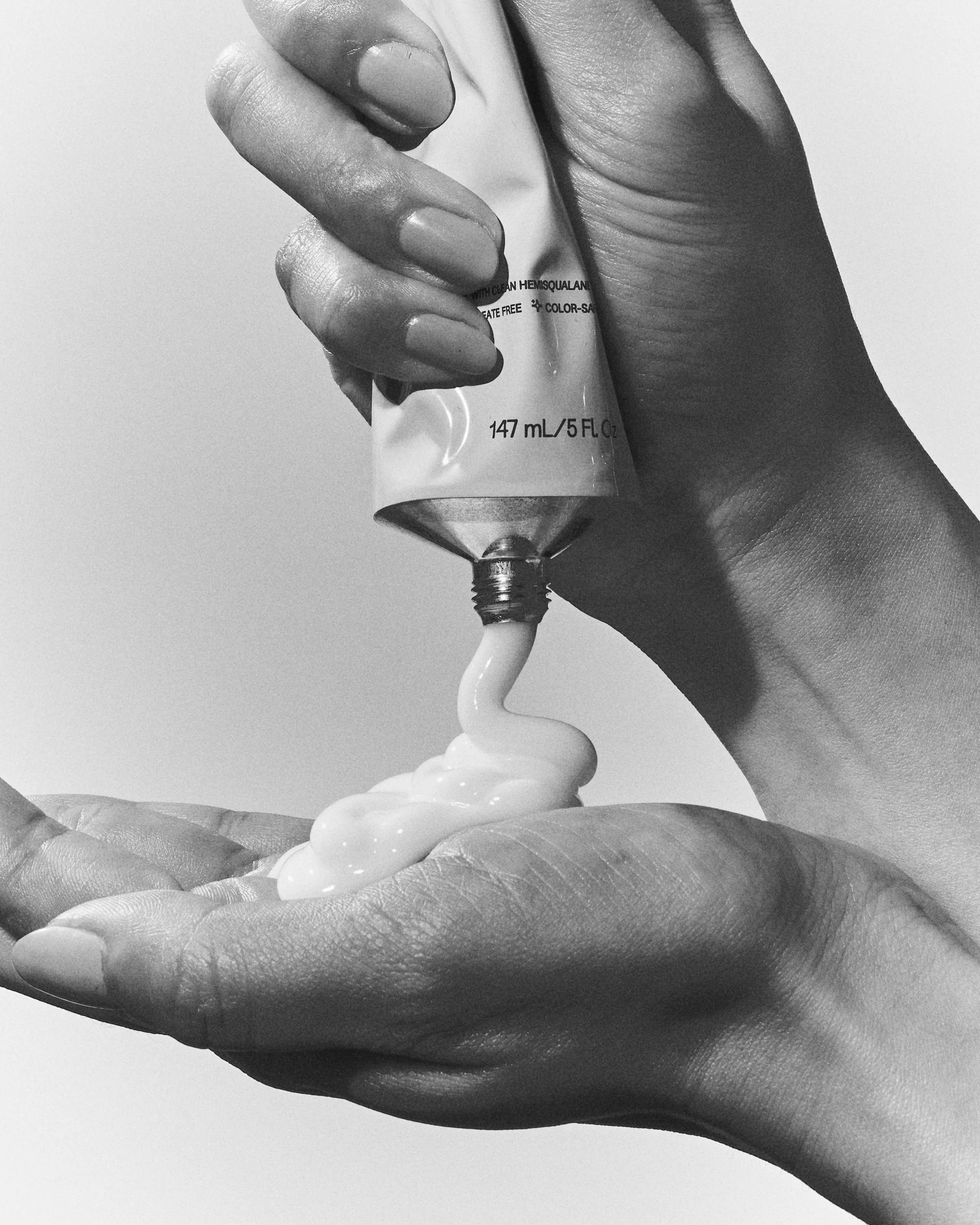 Black and white close-up of hands squeezing white conditioner from a tube into a palm, for JVN.
