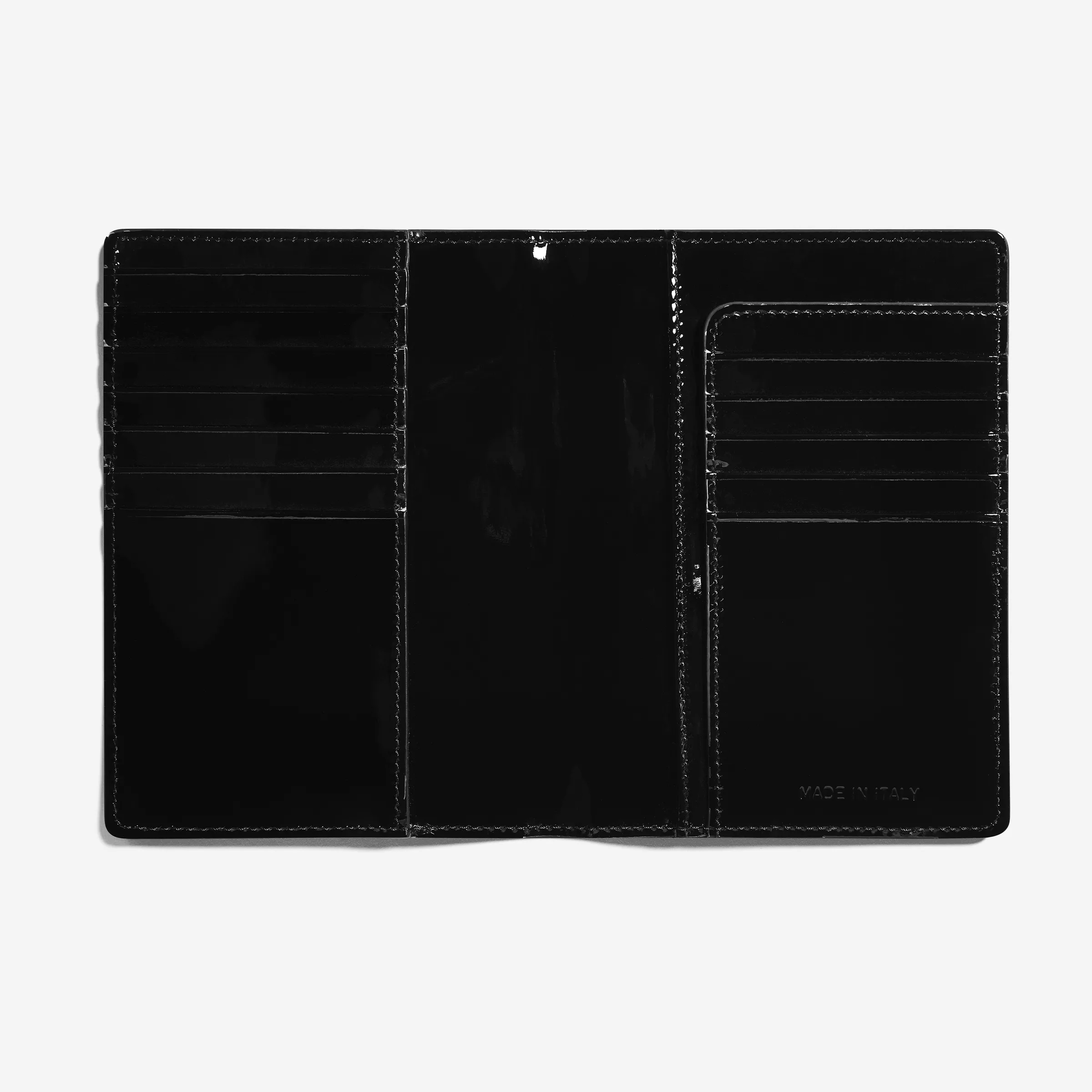 Open black patent leather travel sleeve showing card slots and passport pocket on a light grey background, for Strata.
