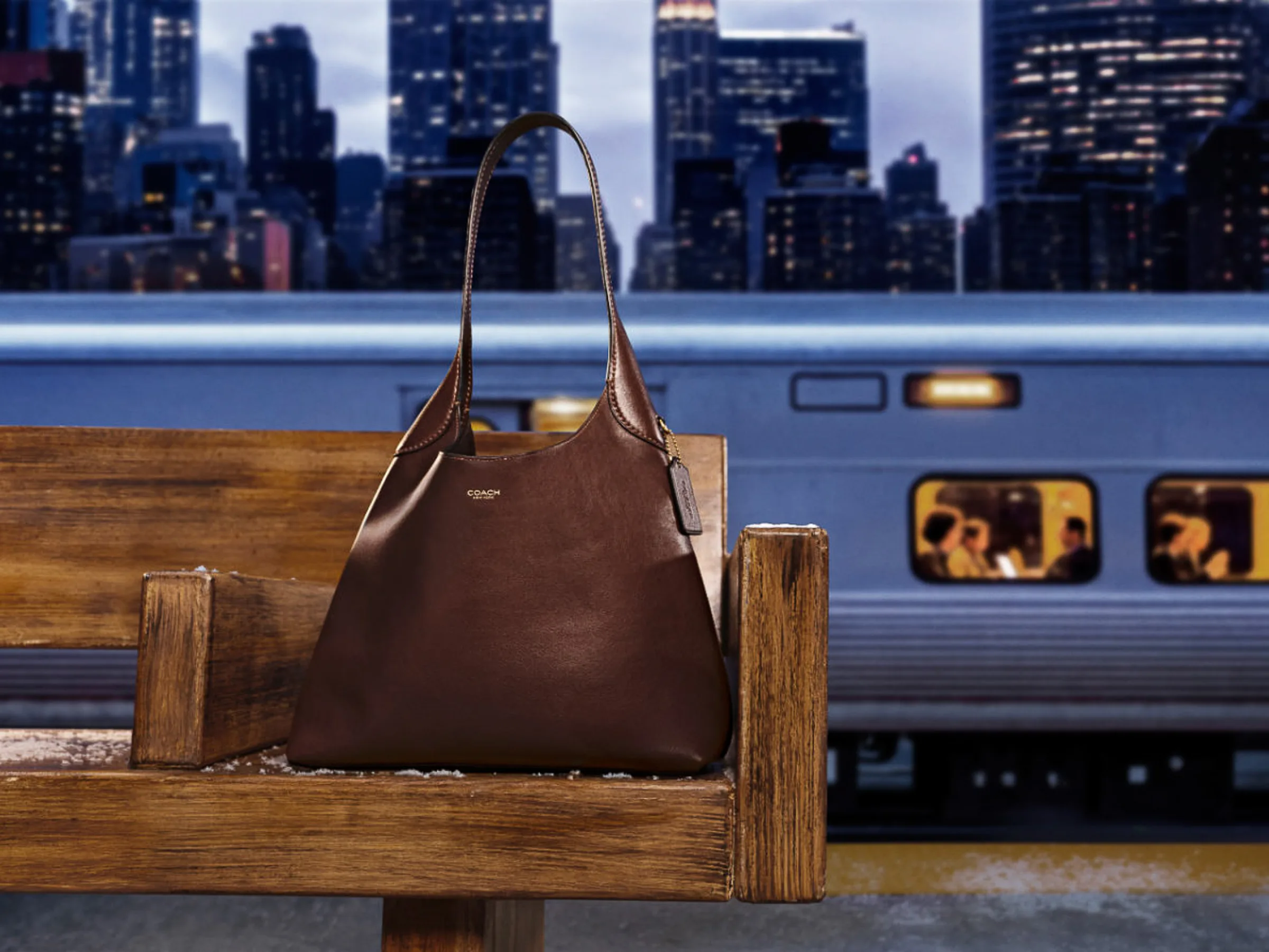 AI image of a brown leather Coach shoulder bag on a wooden bench by a lit commuter train at dusk, city skyline behind, for Coach.