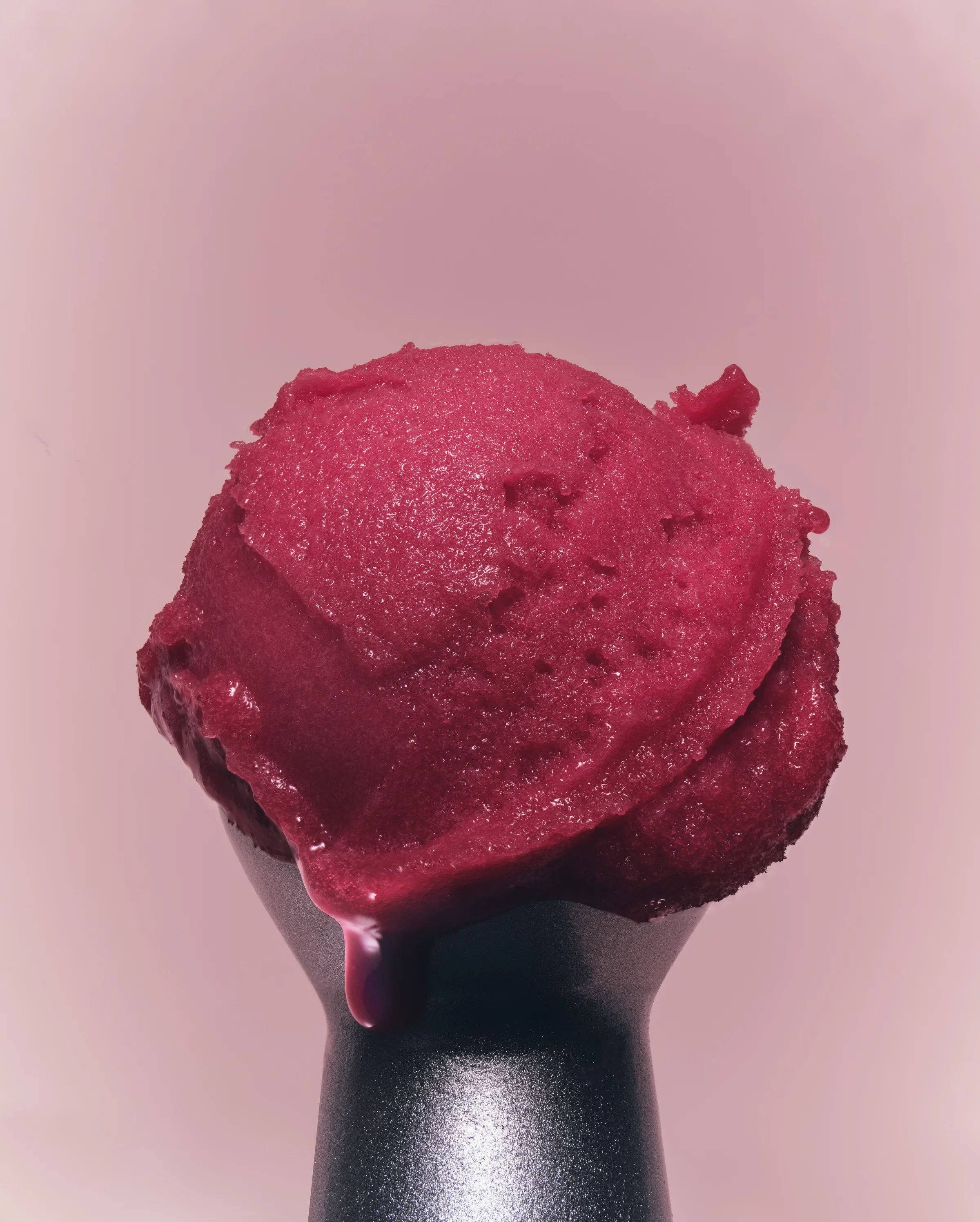 Scoop of deep pink sorbet dripping over a dark metal holder against a muted pink background, for Kylie Cosmetics.