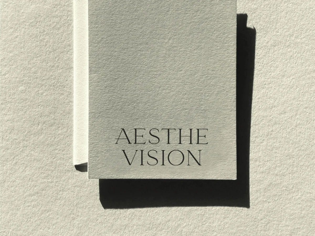 Pale grey textured card printed with the Aesthe Vision wordmark, casting a hard shadow on paper, for Aesthevision.