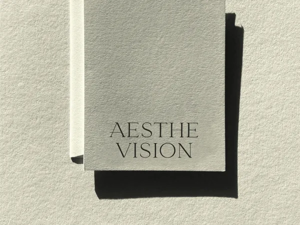 Pale grey textured card printed with the Aesthe Vision wordmark, casting a hard shadow on paper, for Aesthevision.
