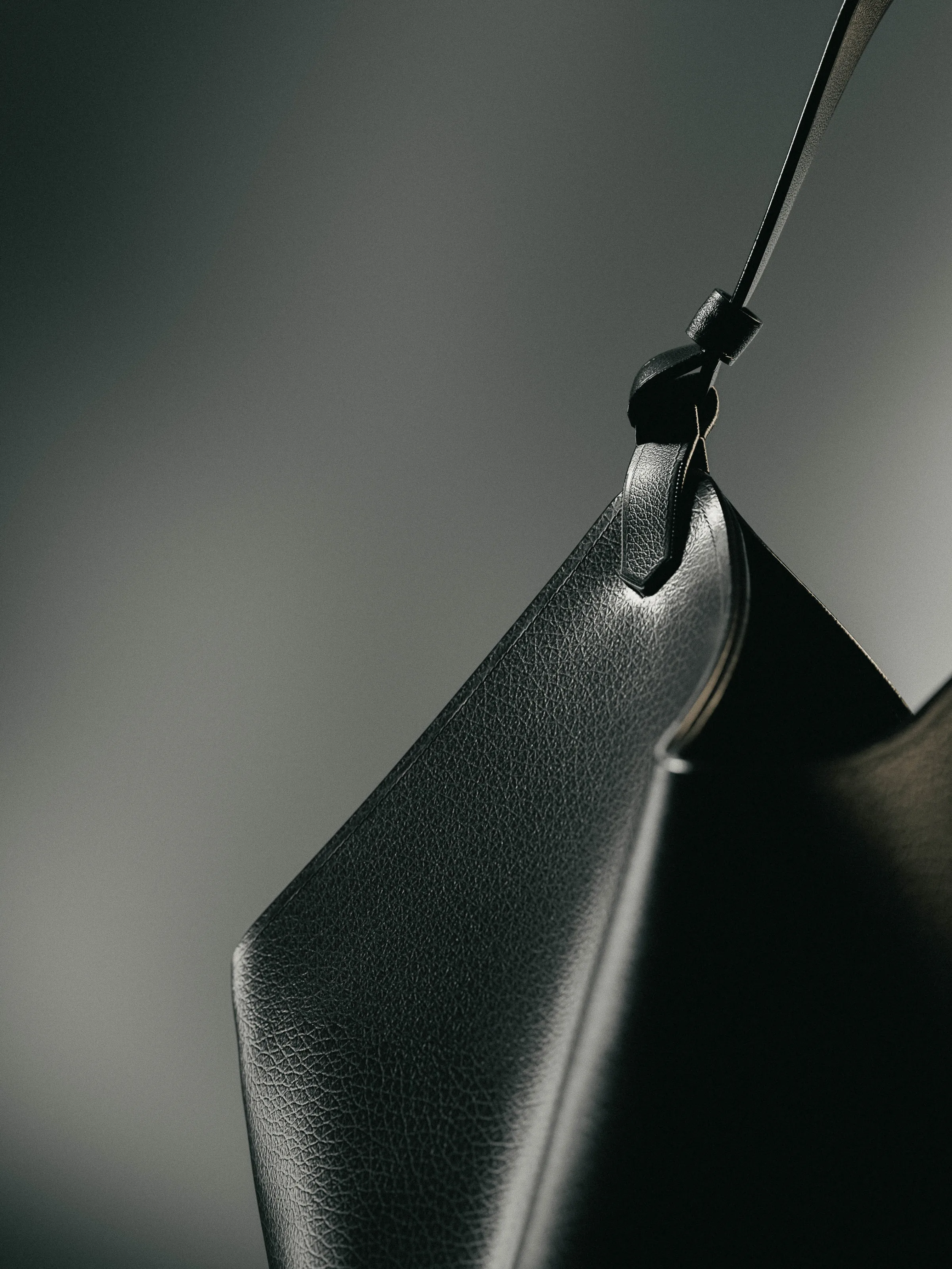 CGI render of a black pebbled leather bag with a knotted strap against a grey gradient, for Khaite.