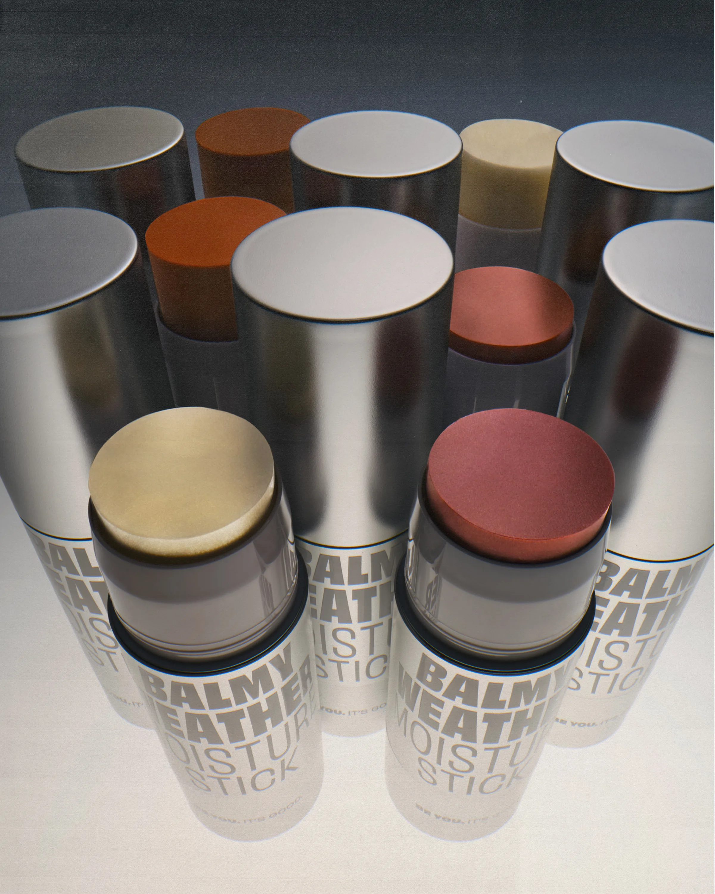 Rows of silver Balmy Weather moisture sticks, some uncapped showing gold, rust and pink balms, for Good Weird.