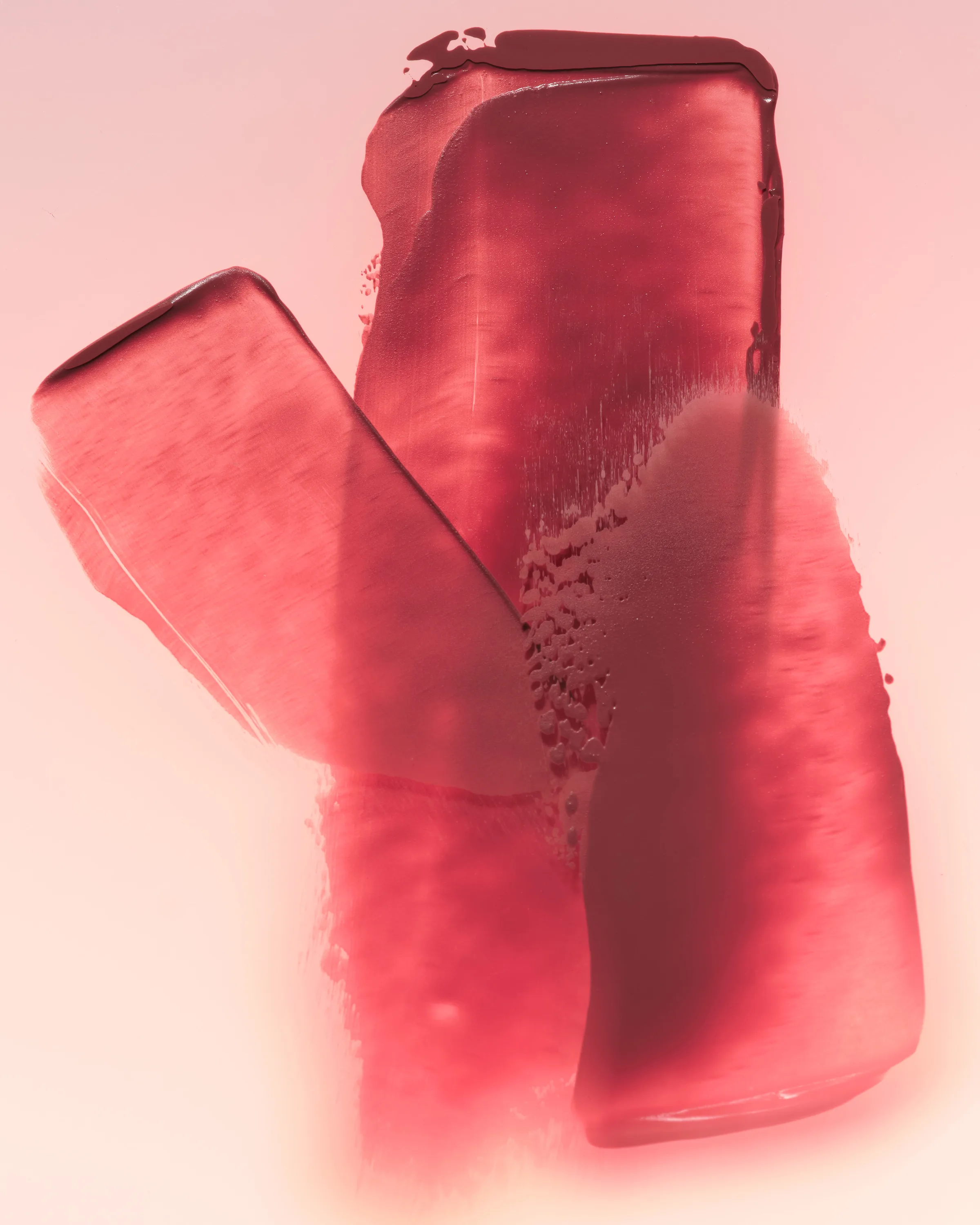 Overlapping swatches of rosy red Love Letter lipstick smeared on a soft pink background, for Kylie Cosmetics.