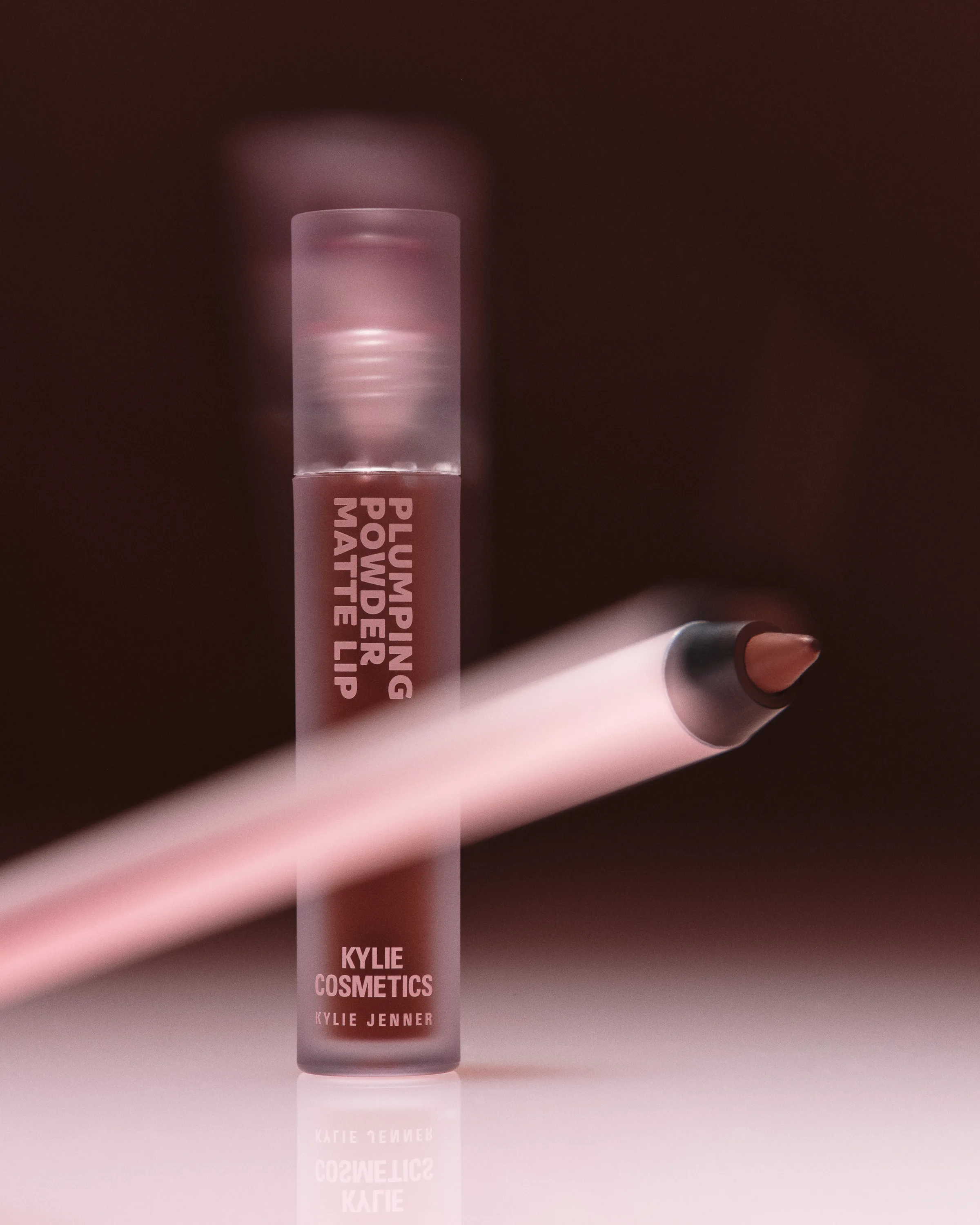 Plumping Powder Matte Lip tube in toffee brown with a motion-blurred pink lip liner on a dark backdrop, for Kylie Cosmetics.