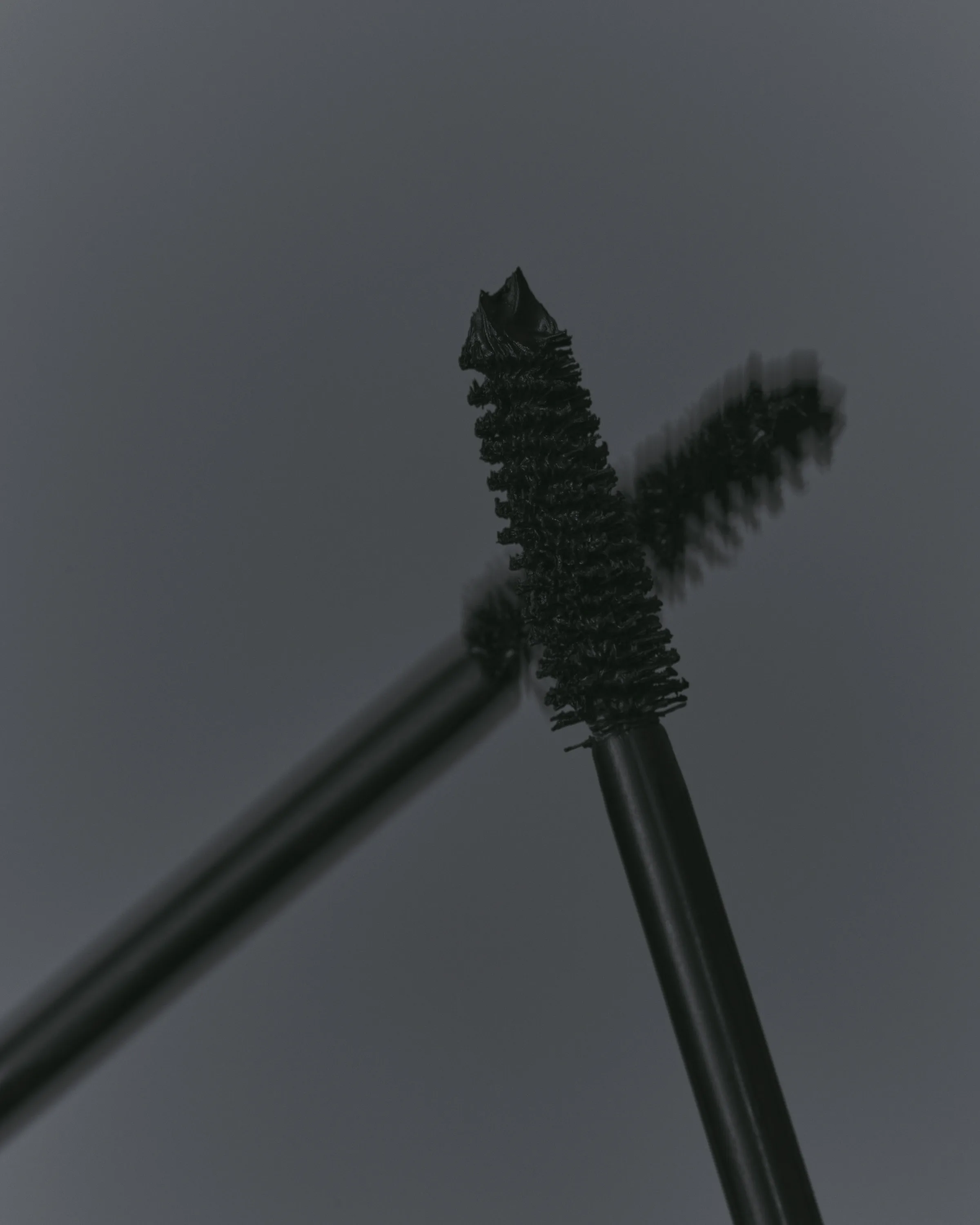 Two black mascara wands crossing against a grey background, one sharp and one motion-blurred, for Kylie Cosmetics.