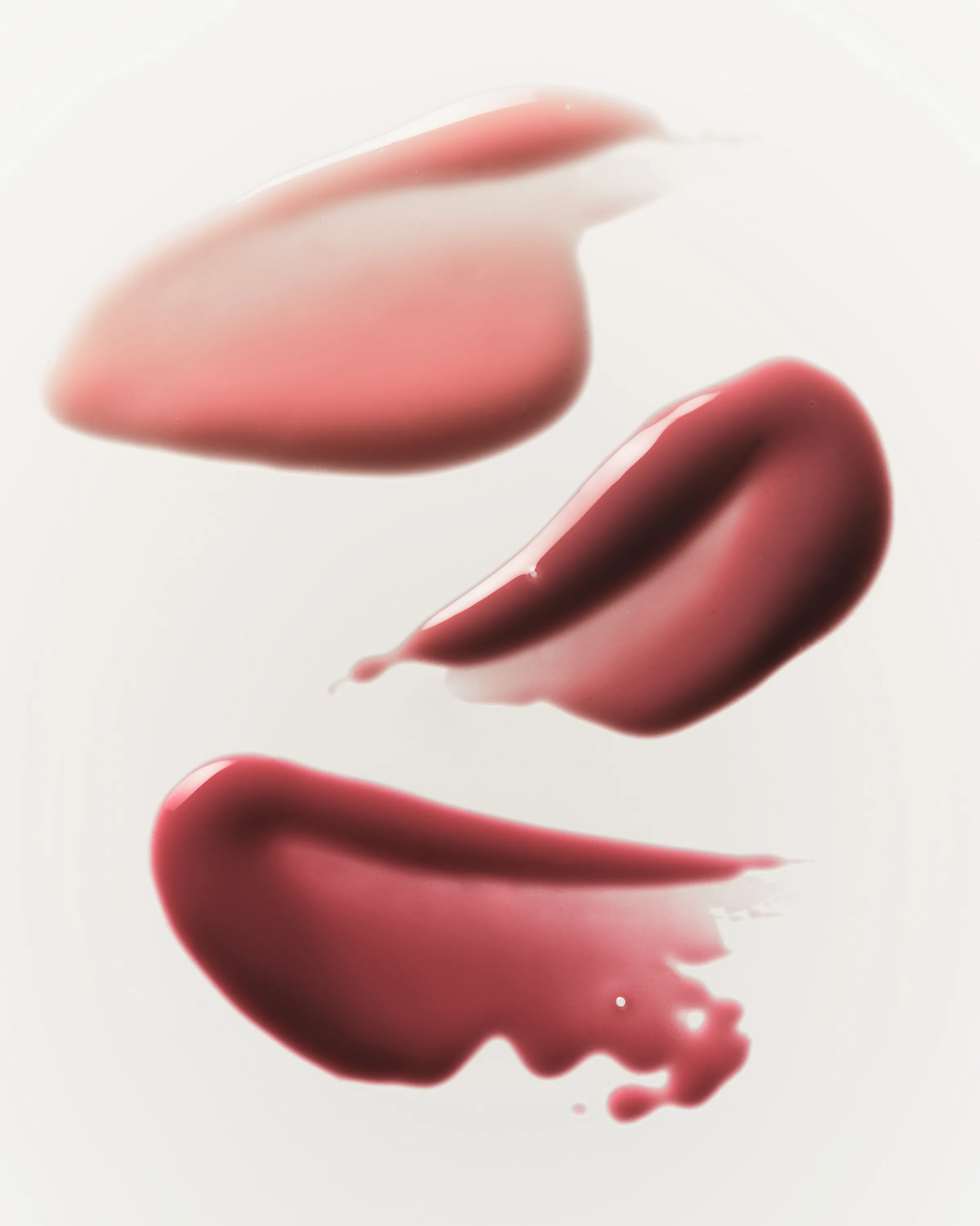 Three lip gloss swatches in nude pink, berry and rose red smeared across a white background, for Kylie Cosmetics.