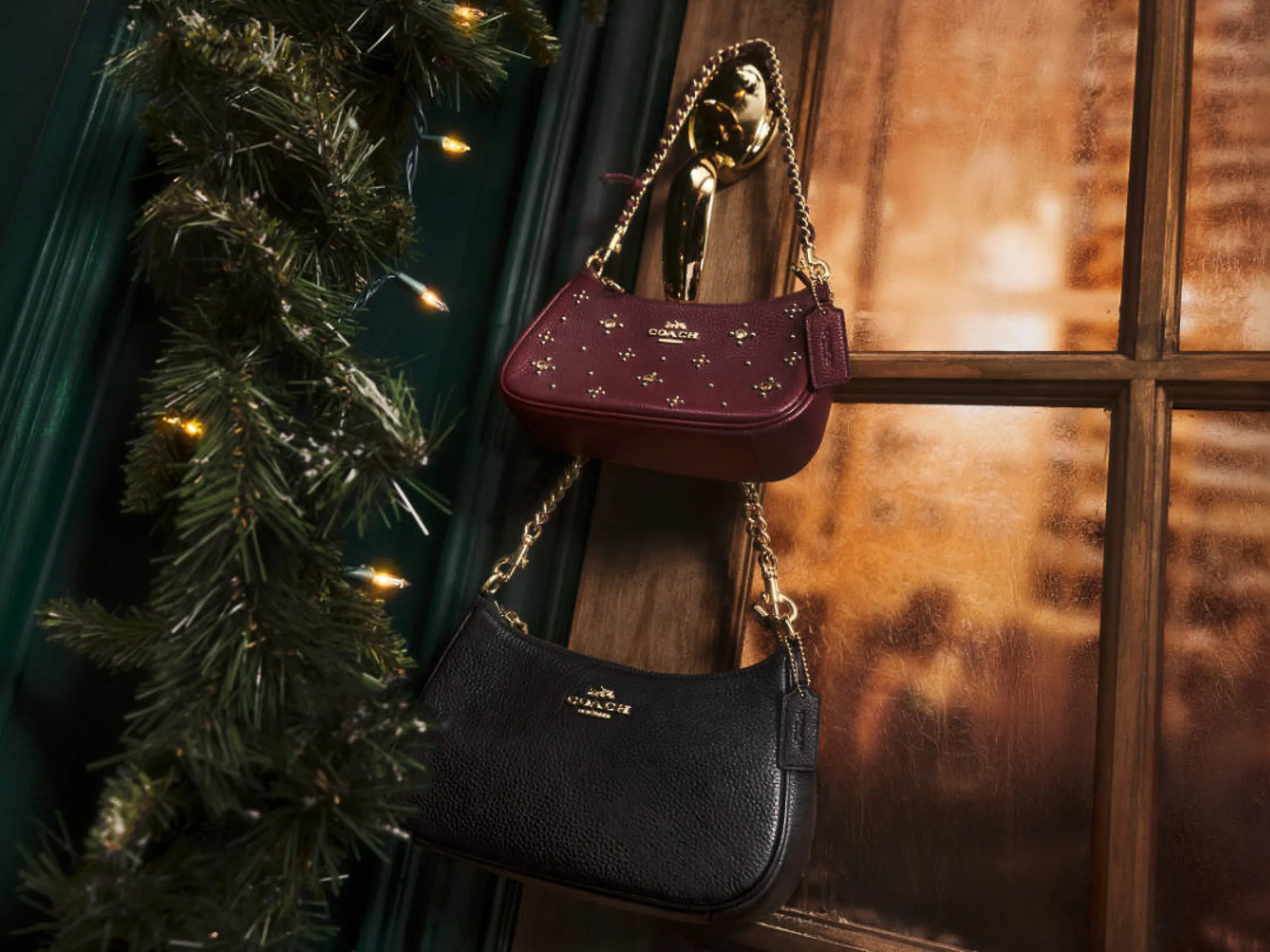 AI image of burgundy studded and black leather Coach shoulder bags hanging on a door handle beside a lit garland, for Coach.