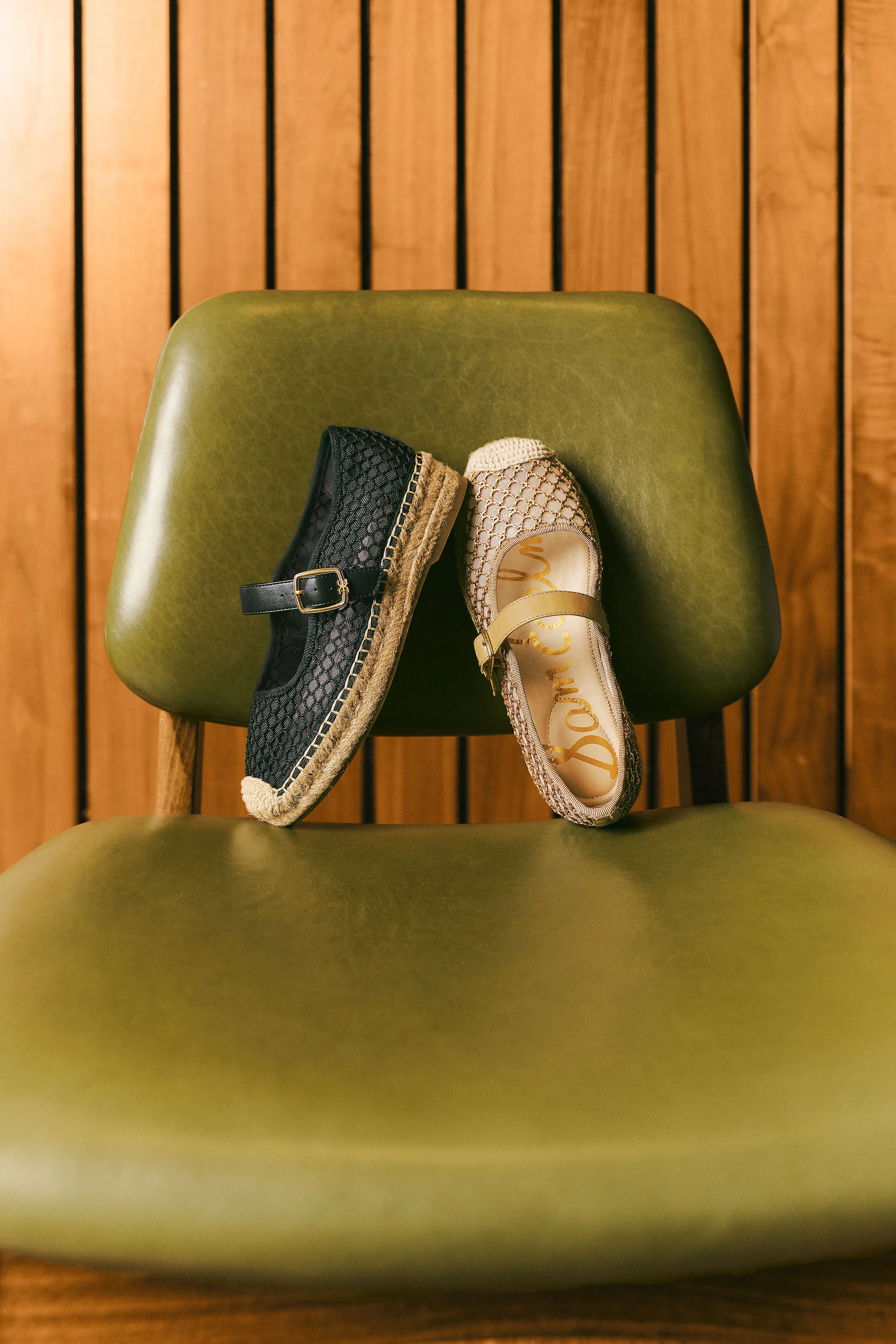 Black and natural mesh espadrille Mary Janes resting on a green leather chair against wood slats, for Sam Edelman.