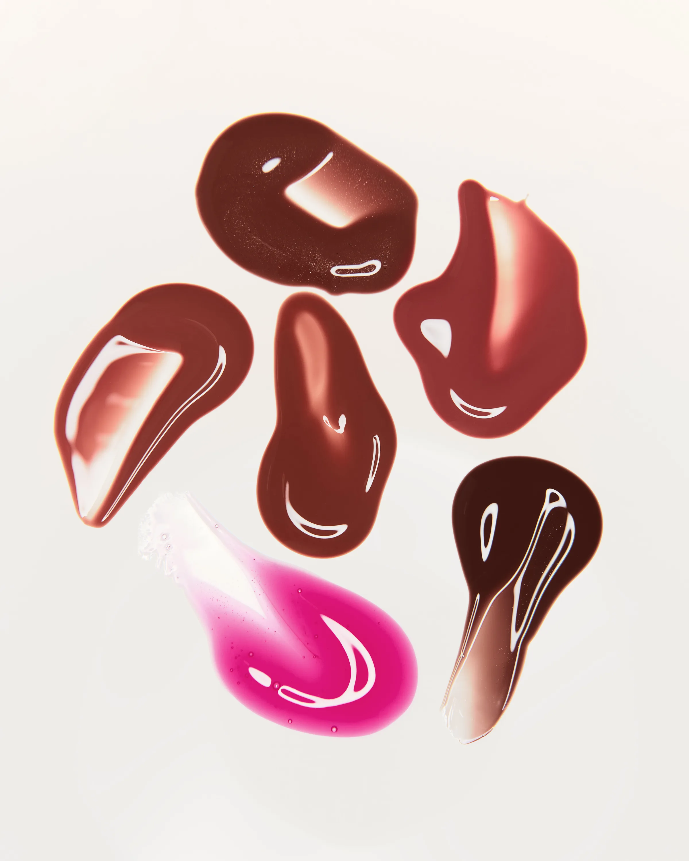 Glossy lip glaze swatches in brown, berry and bright pink shades on a white background, for Kylie Cosmetics.