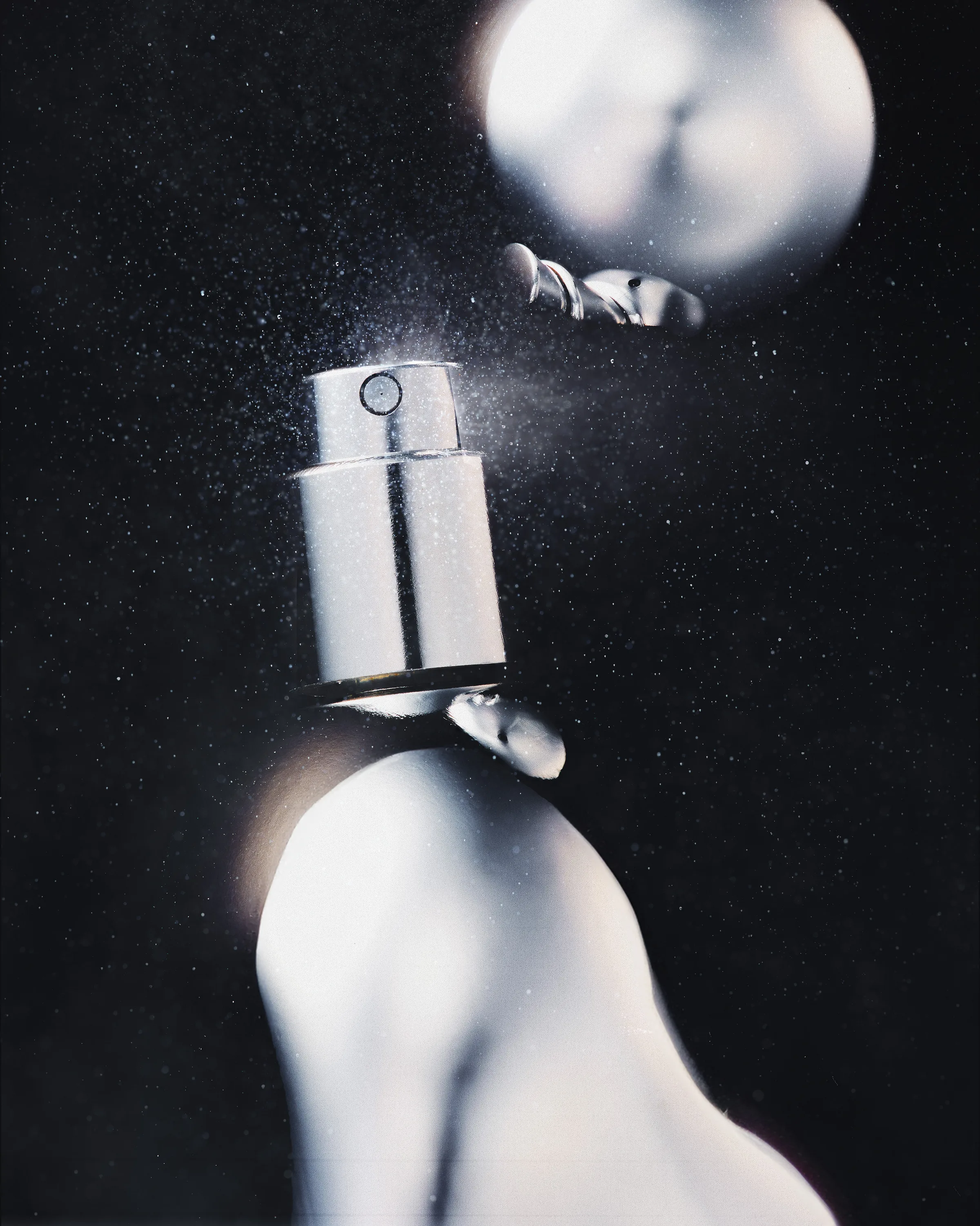 Silver perfume bottle releasing a fine mist against a dark, speckled background, for Kylie Cosmetics.